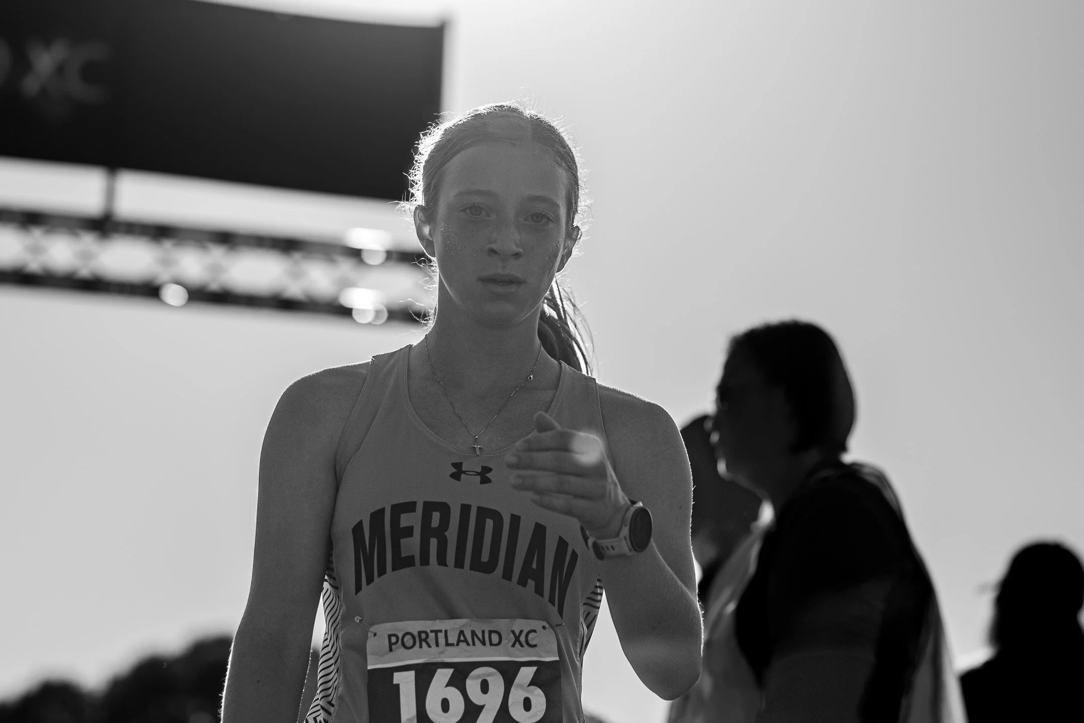 Black-and-white close-up of Meridian sophomore Bria Rempp with one hand extended, bib 1696, backlit against a bright sky.