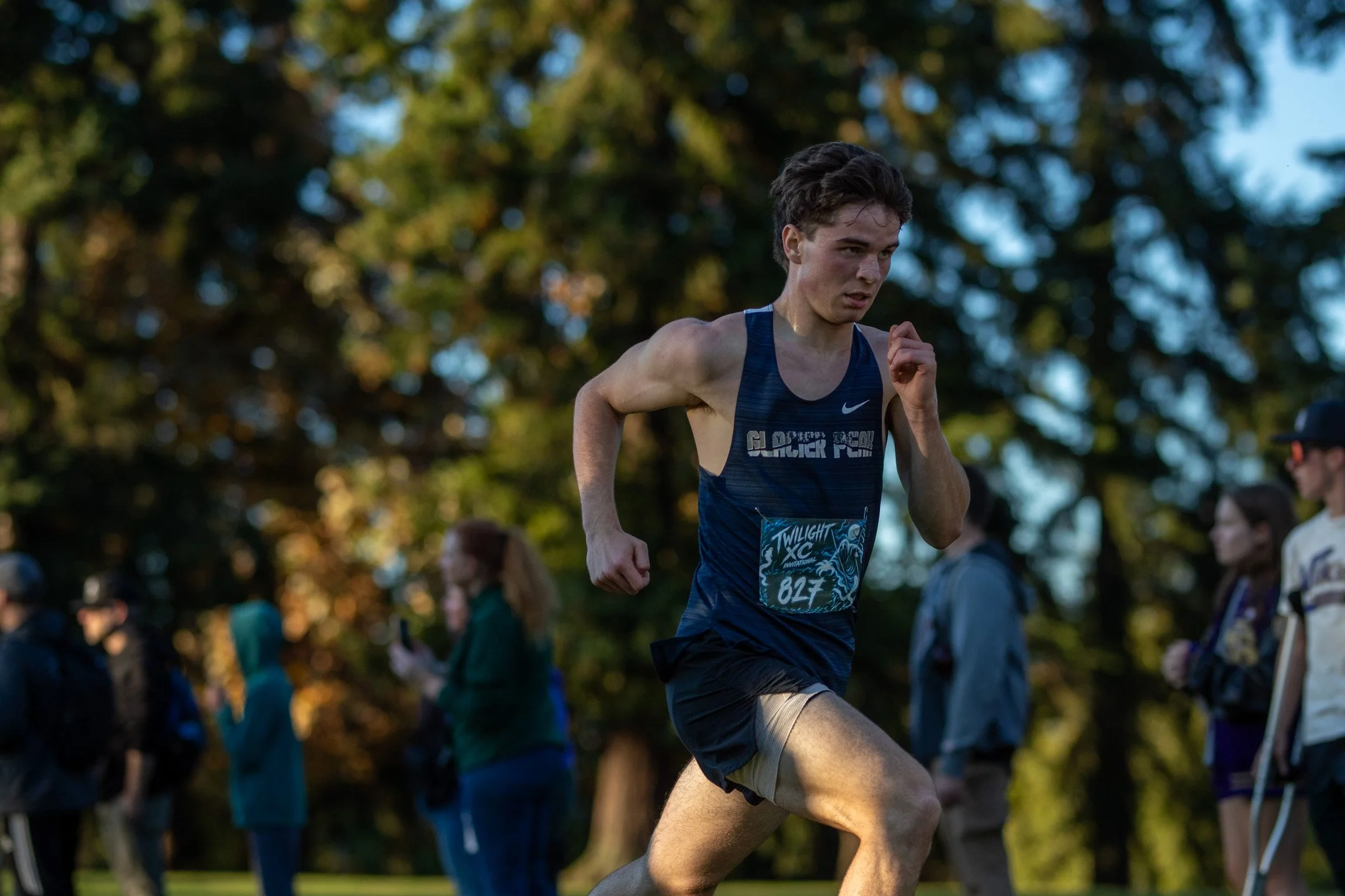 Glacier Peak runner Blake Roberts in a navy uniform with bib 827 running hard across the grass fairway in late-day sunlight.