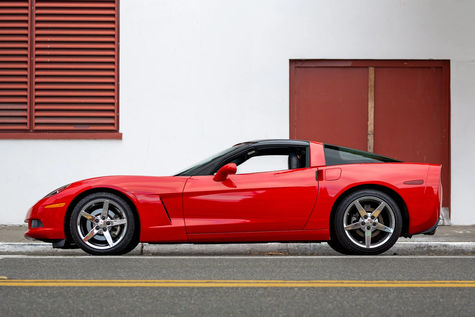 Side view of a red 2005 Chevrolet Corvette C6 coupe parked on a street, showcasing its classic sports car design.