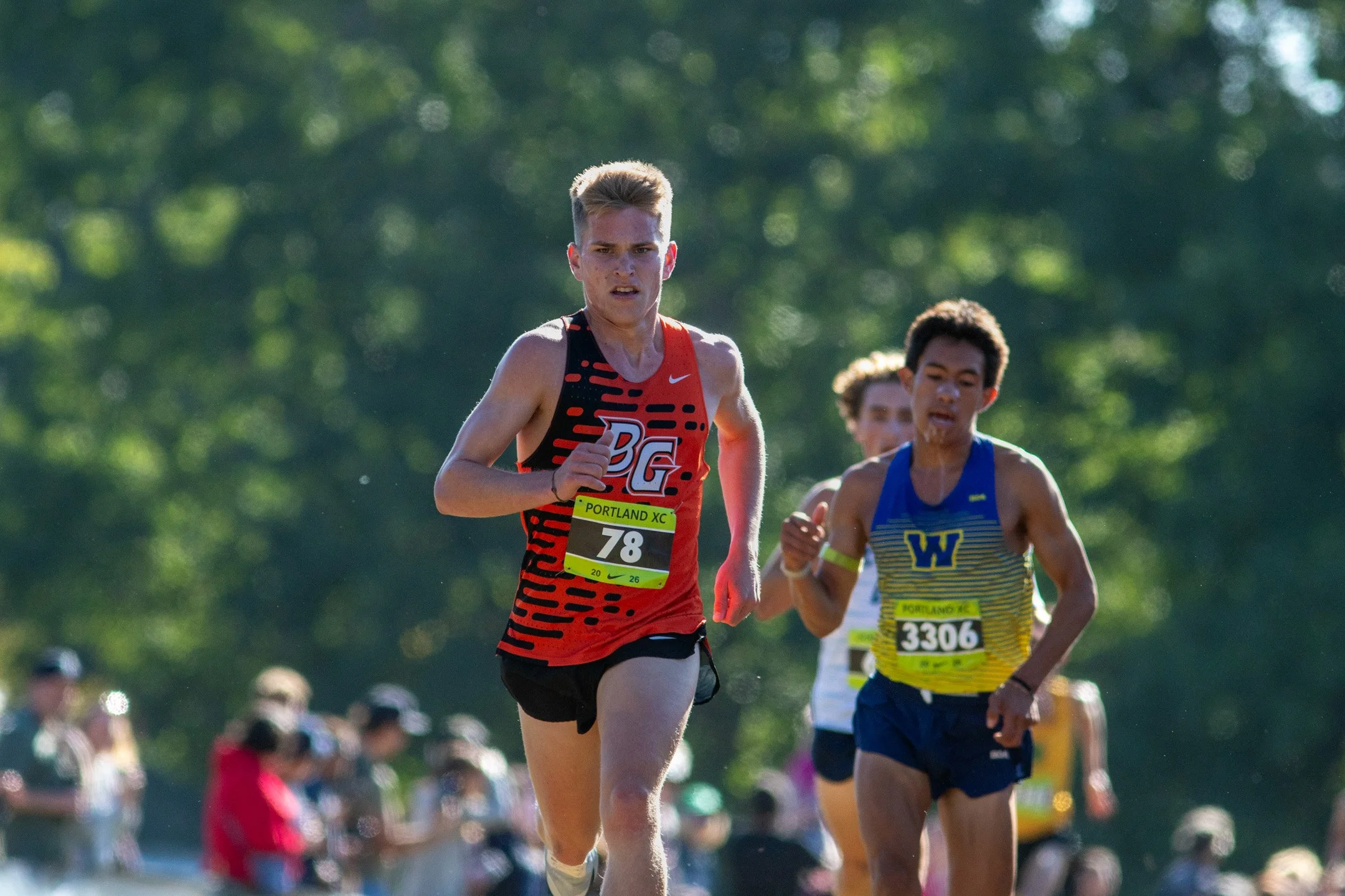 Battle Ground senior Trae Copper in a red singlet, bib 78, runs beside a runner in a blue and yellow jersey, crowd blurred behind.