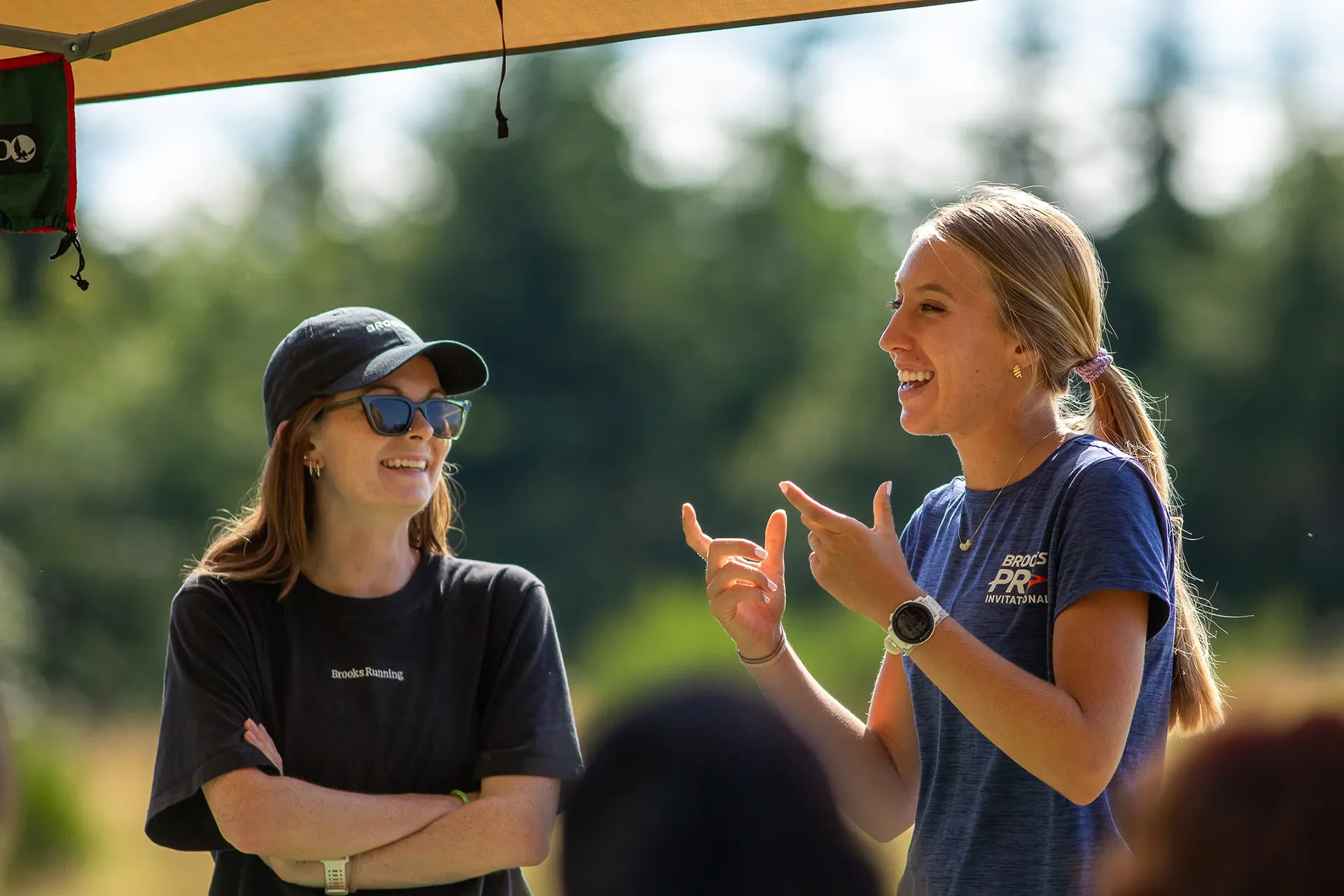 Two women, Alexa Matora and Caroline Daniel, smiling and talking to an out-of-focus crowd outdoors.