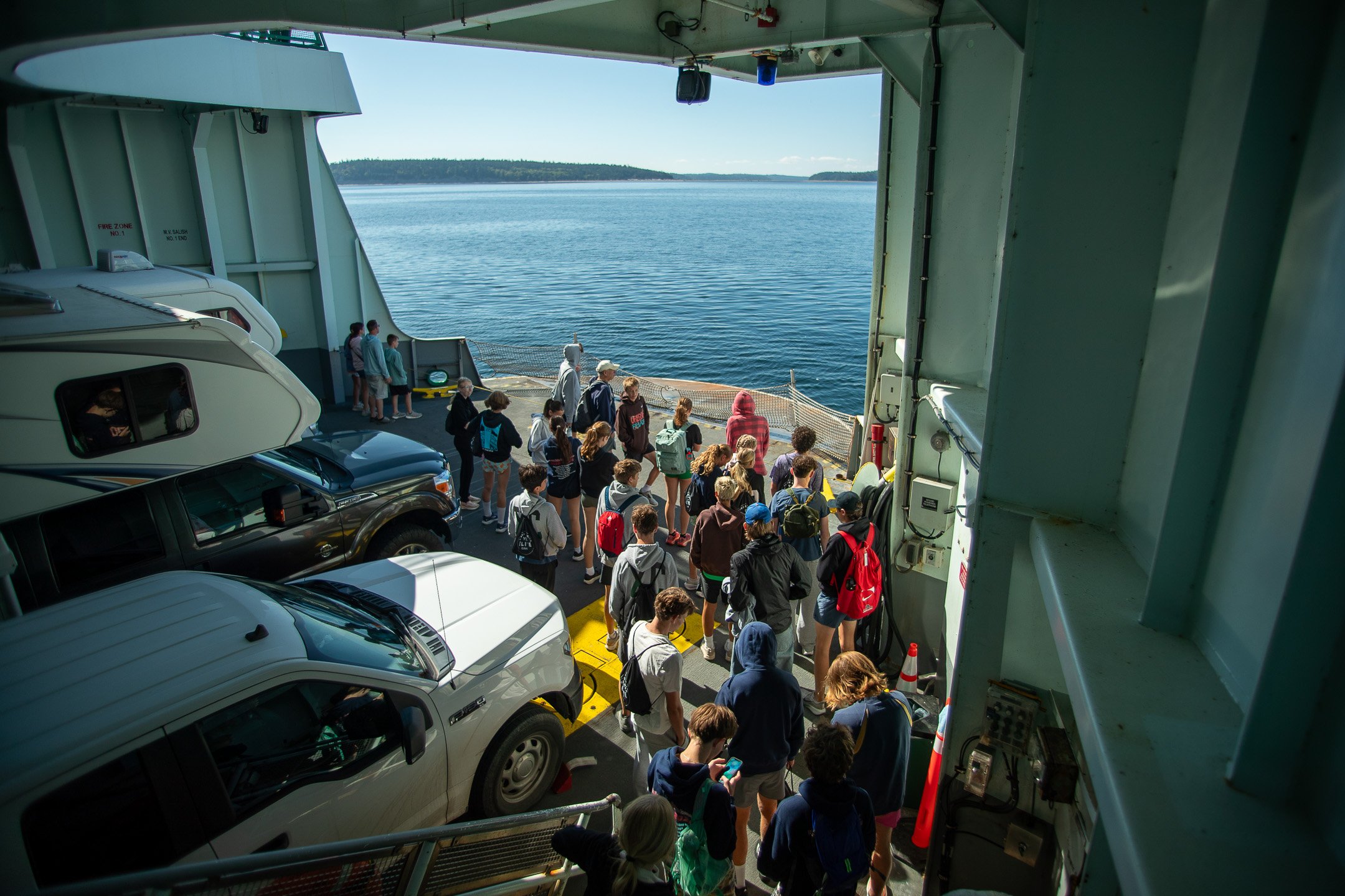 High school cross country campers and coaches gather on the deck of a Washington State Ferry looking out over the water as the ferry approaches the Port Townsend dock.