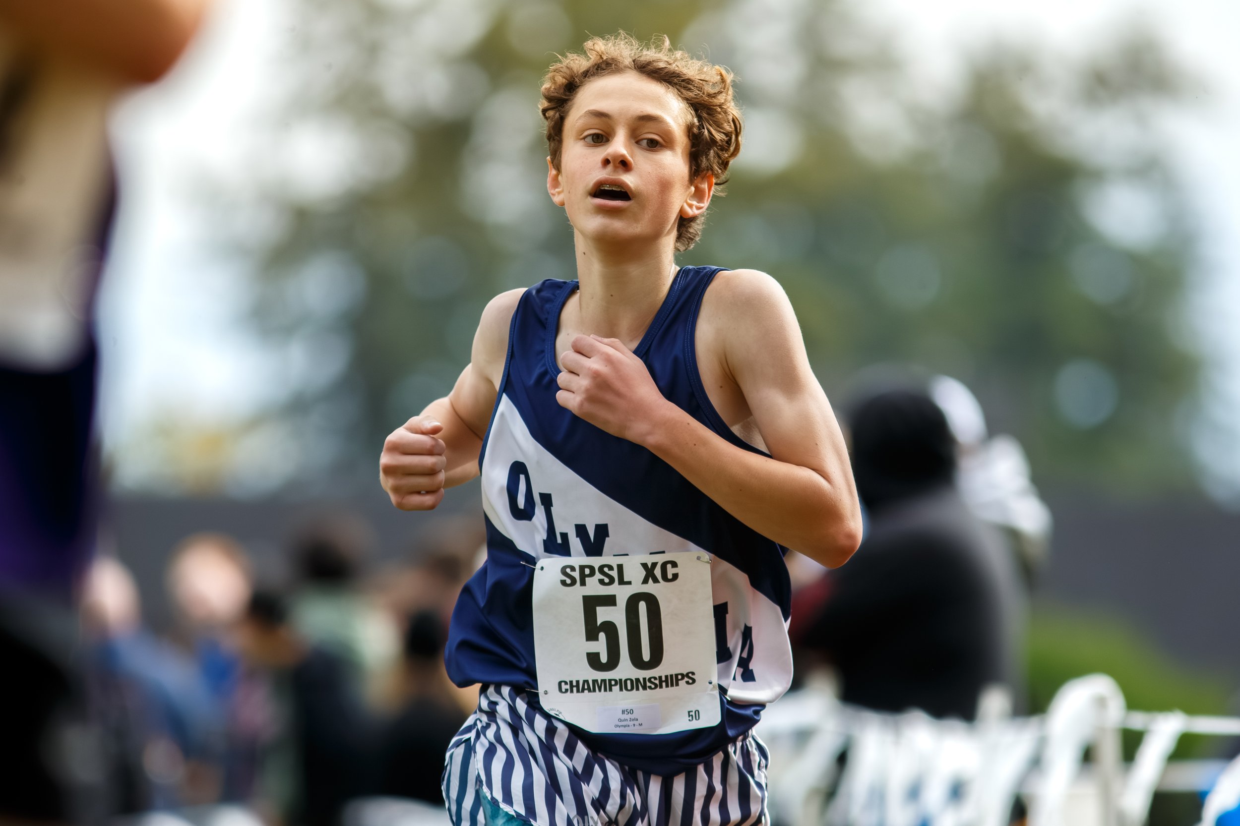 Quin Zola of Olympia High School finishing the varsity race at the 2025 SPSL 4A League Championships at Fort Steilacoom, wearing a navy and white Olympia uniform.