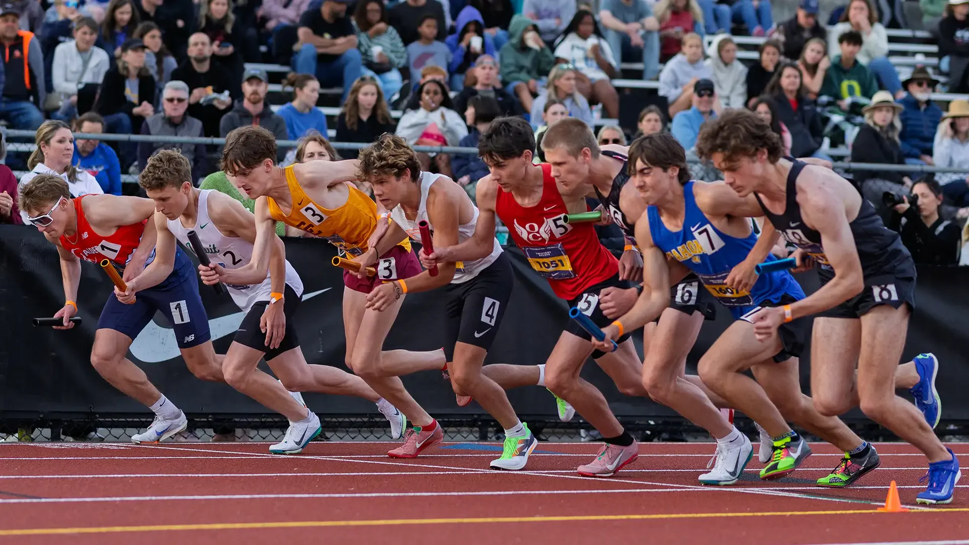 High-speed action photography of the boys relay start at the Jesuit Nike Twilight track meet in Portland, Oregon. Runners are shown driving hard out of the starting blocks, digging into the track as the race begins.