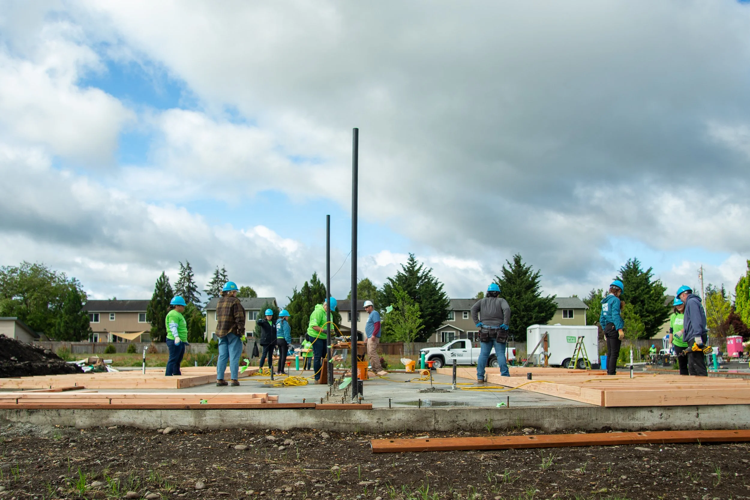 A wide-angle landscape shot of a residential construction site in Yelm showing the progress made on a wooden house frame at the end of a build event.