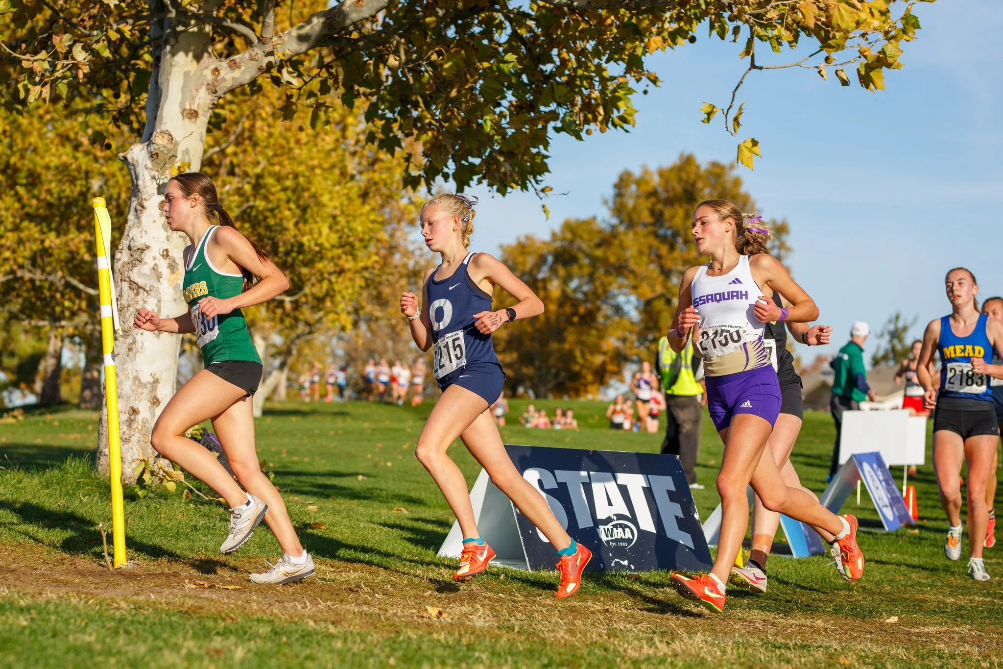 Eliza Johnson of Olympia High School rounding a corner at the 2025 WIAA XC State Championships in Pasco, Washington, running alongside competitors.