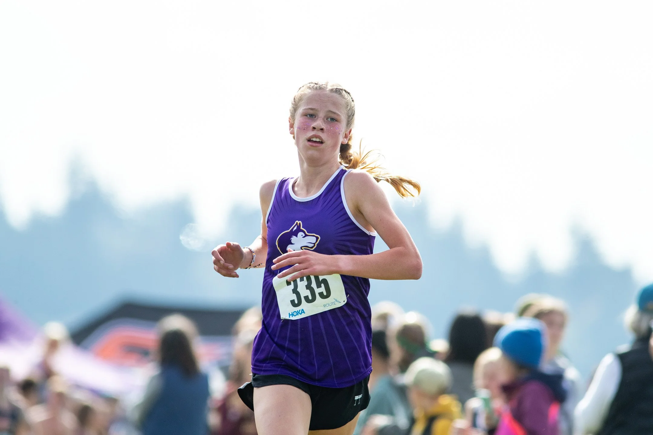 Sequim High School runner Eleanor Jones in a purple jersey with bib 335 sprinting down the final straightaway with focus.