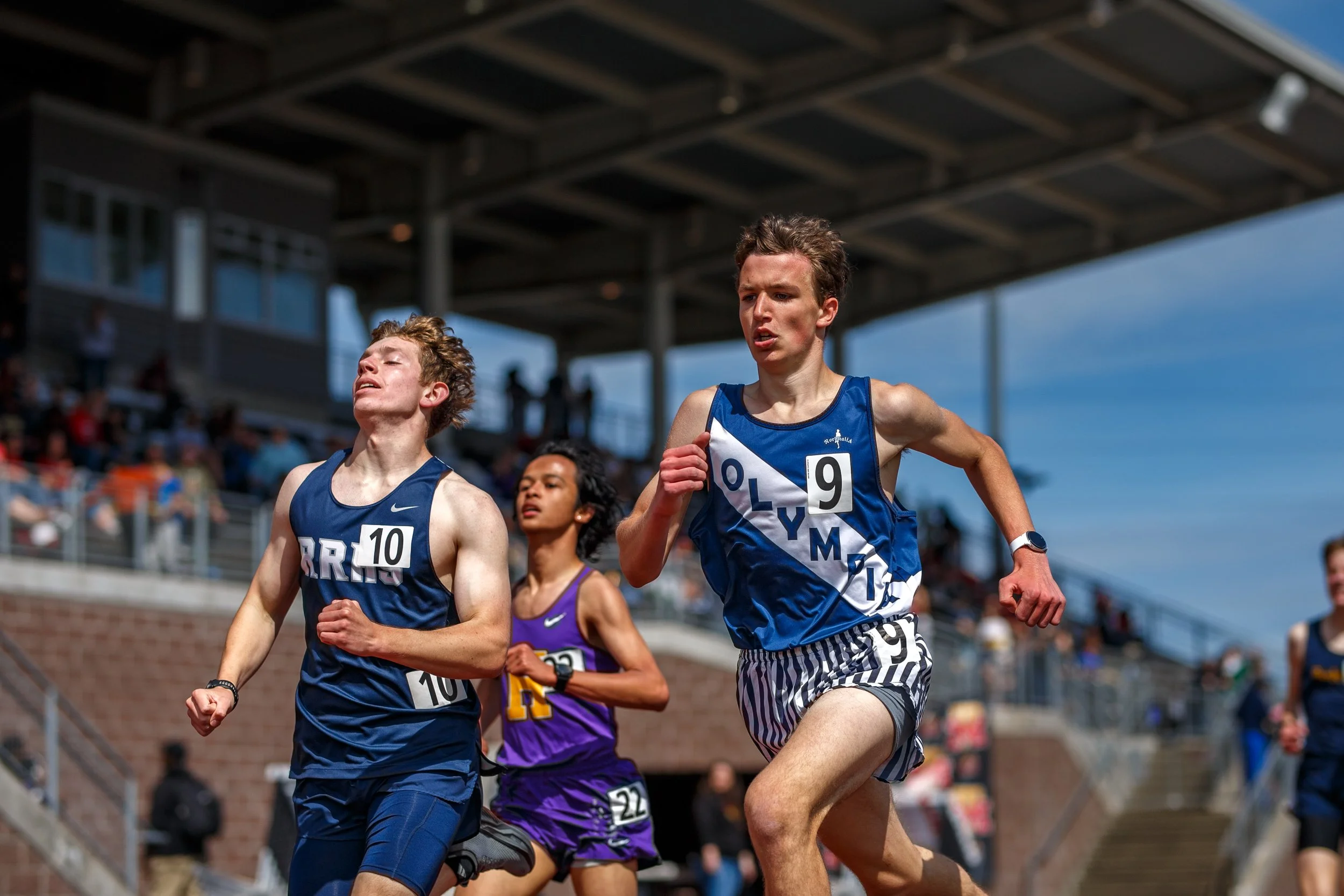 Liam Doyle of Olympia High School passing a River Ridge competitor during a race at the Mt. Tahoma Track Festival, wearing a navy Olympia singlet.