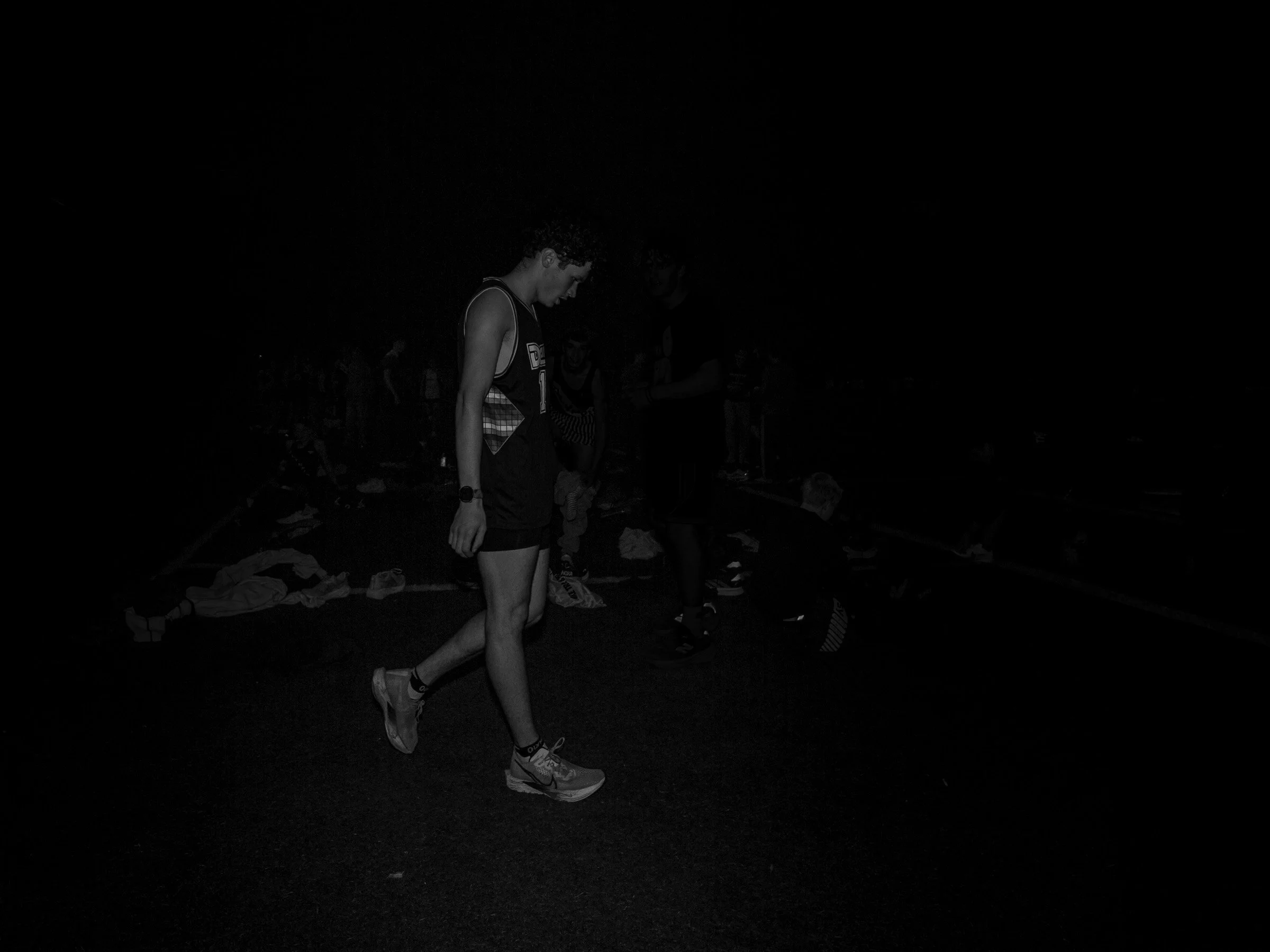 Senior runner walking with head bowed after a race at night.