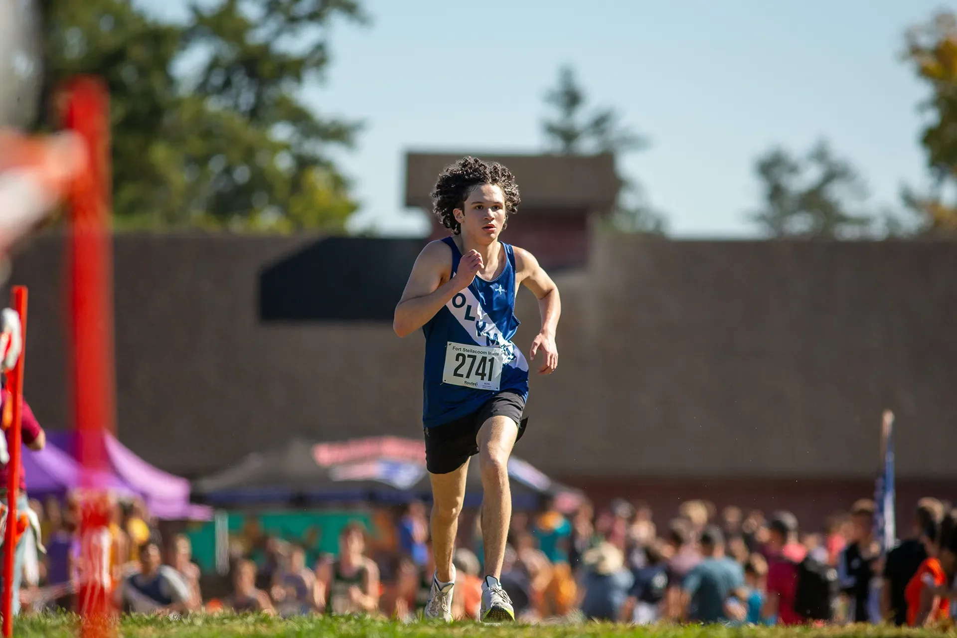 Ephraim Moore of Olympia High School cresting a hill during a cross country race at Fort Steilacoom, wearing a navy and white Olympia uniform.