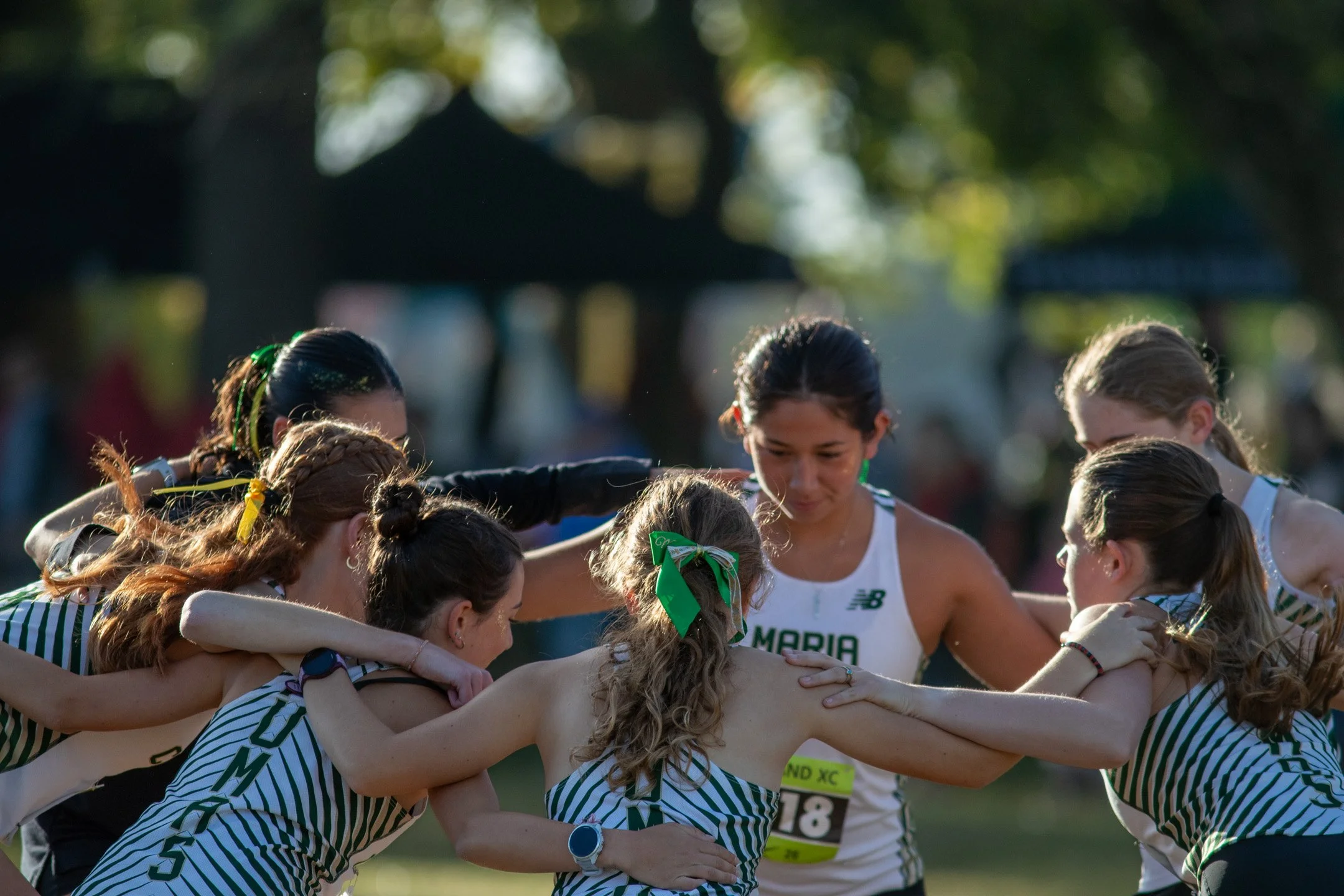 Maria Carrillo runners lock arms in a tight team huddle before the opening race, one girl in sharp focus at center.