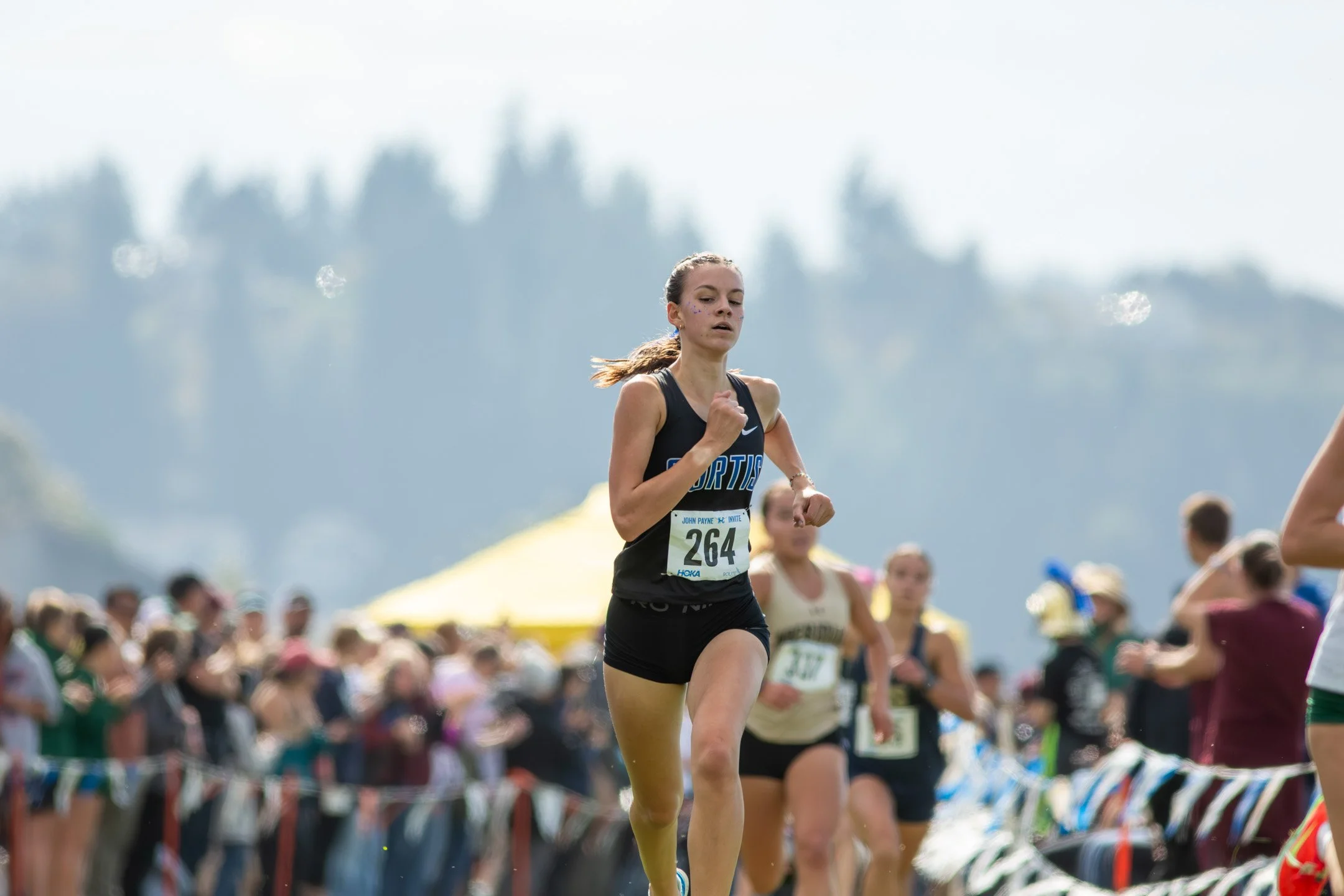 High school girl running alone through spectators lining the course.