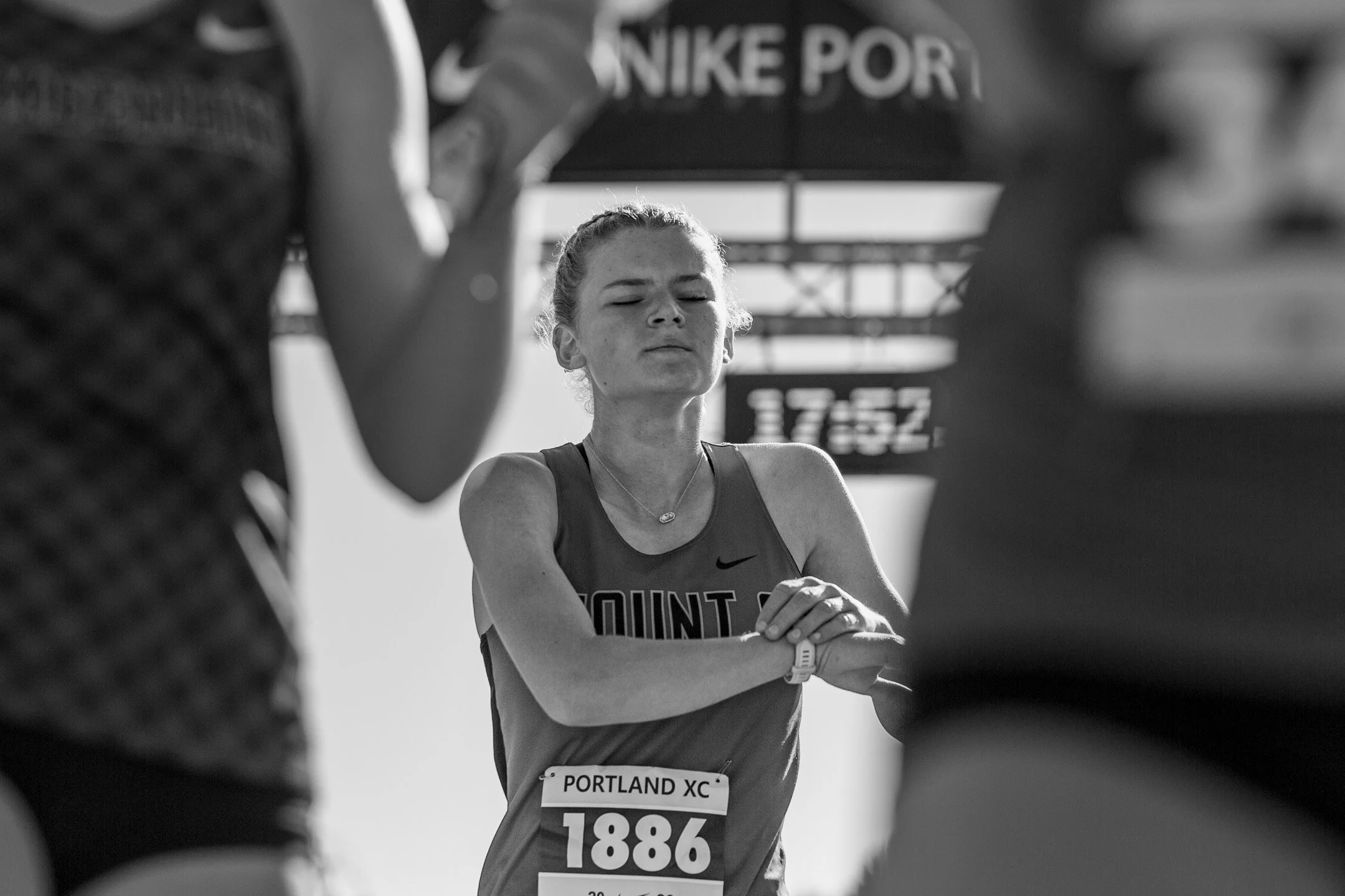 Black-and-white image of Mt. Si senior Ryan Mclellan, eyes closed, a hand on her watch just after finishing, the race clock blurred behind her.