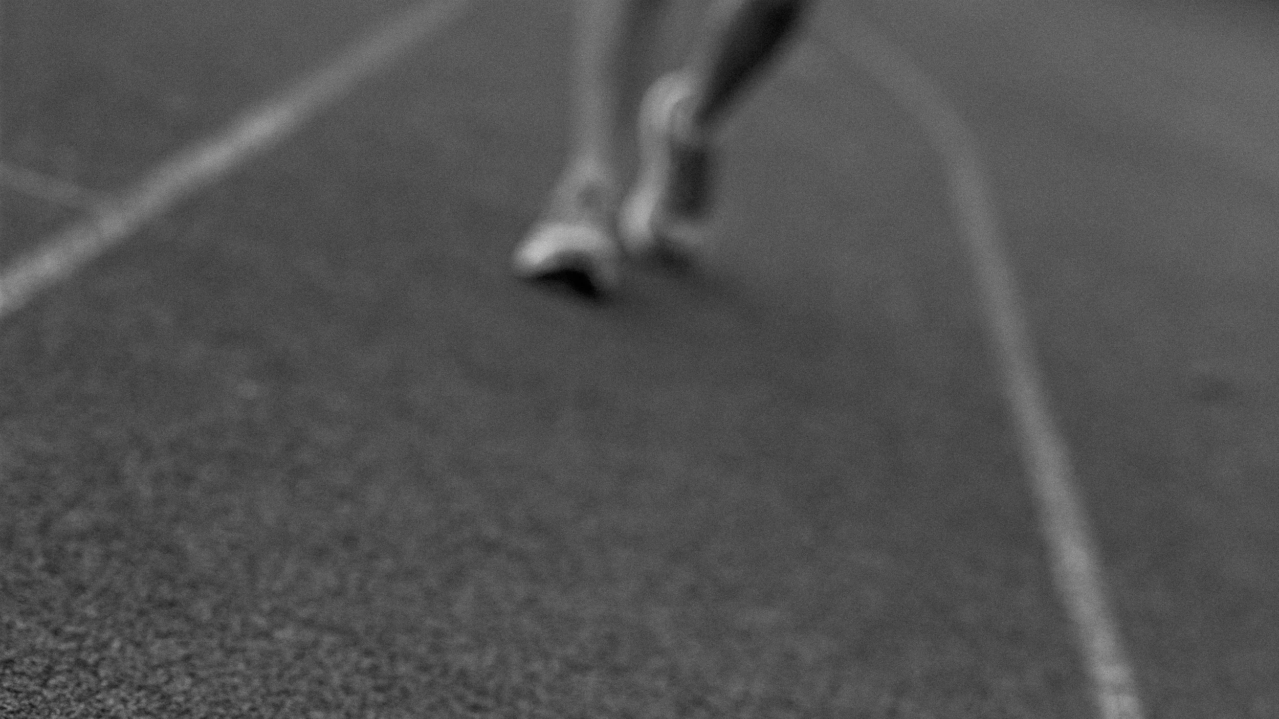 Motion blur black and white photo of a runner's shoes on a track, representing the hard work of off-season running.