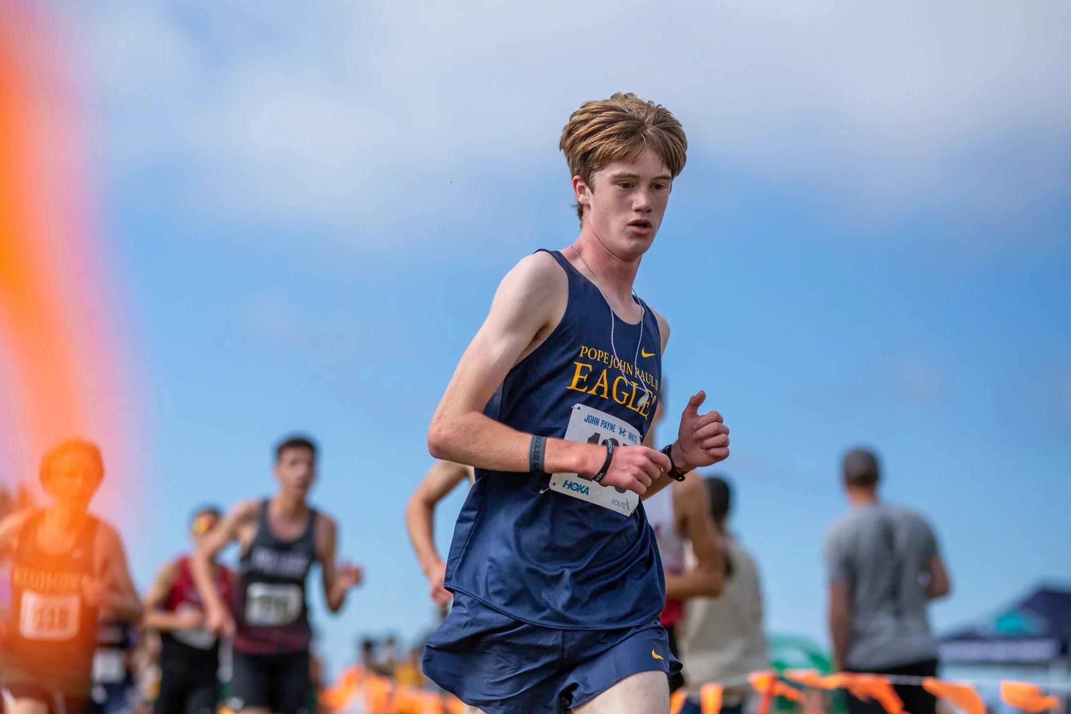 Pope John Paul II freshman Micah Henry running mid-race in a navy blue and gold uniform along the Chambers Creek course.