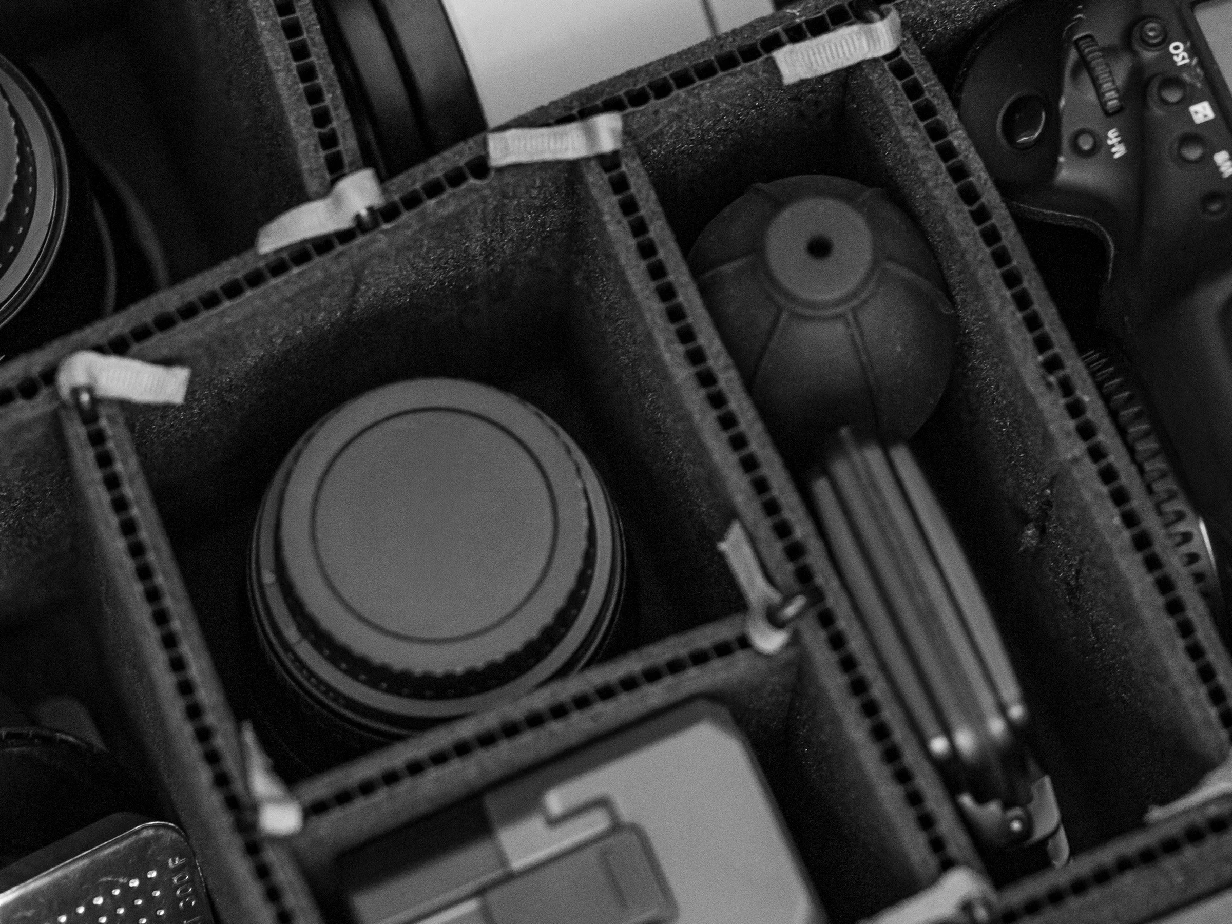 Overhead view of an open camera bag with padded dividers holding a lens, a camera body, and a blower.