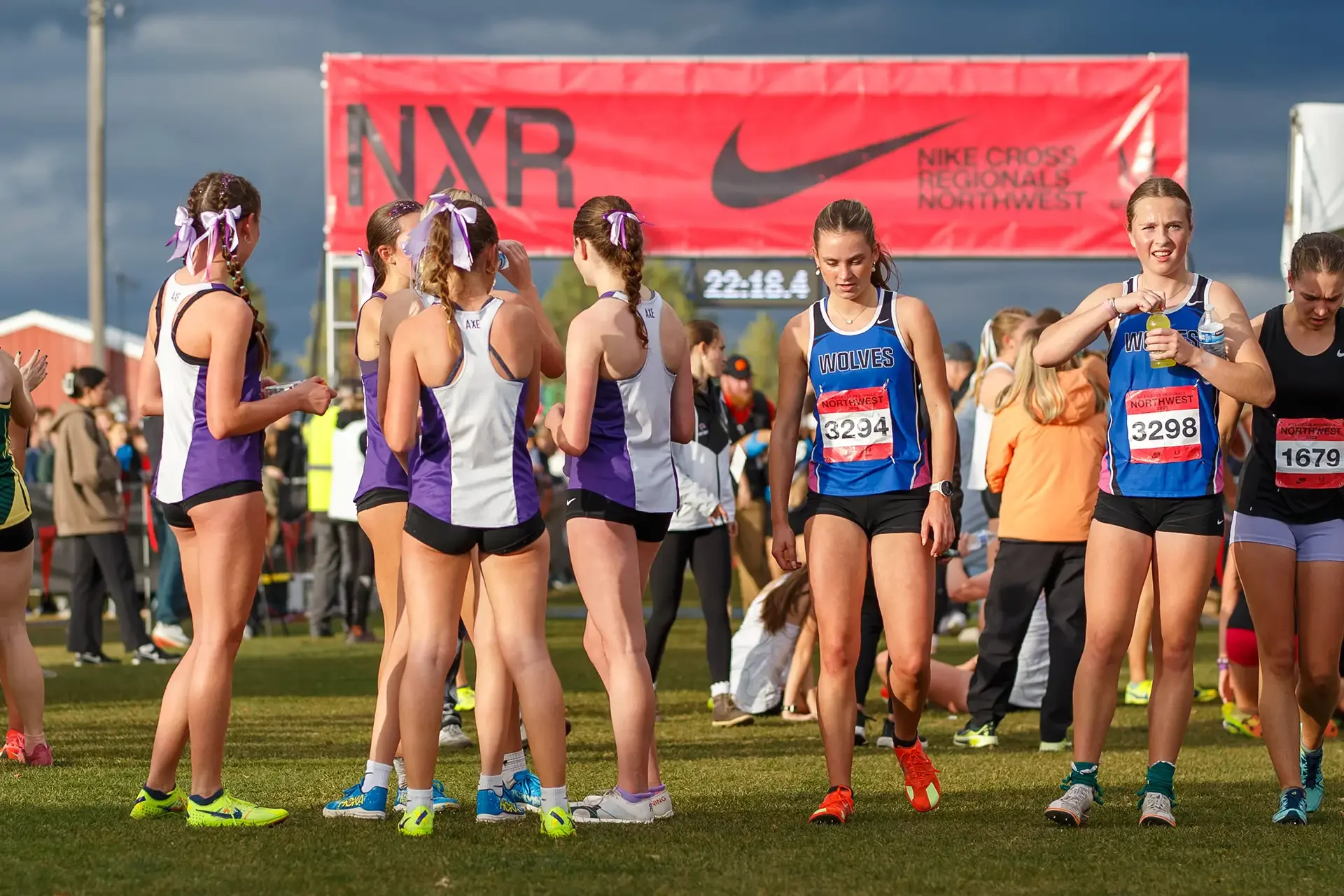A large group of female cross-country runners in various team uniforms gathering and preparing to race in front of a red Nike Cross Regionals Northwest banner.