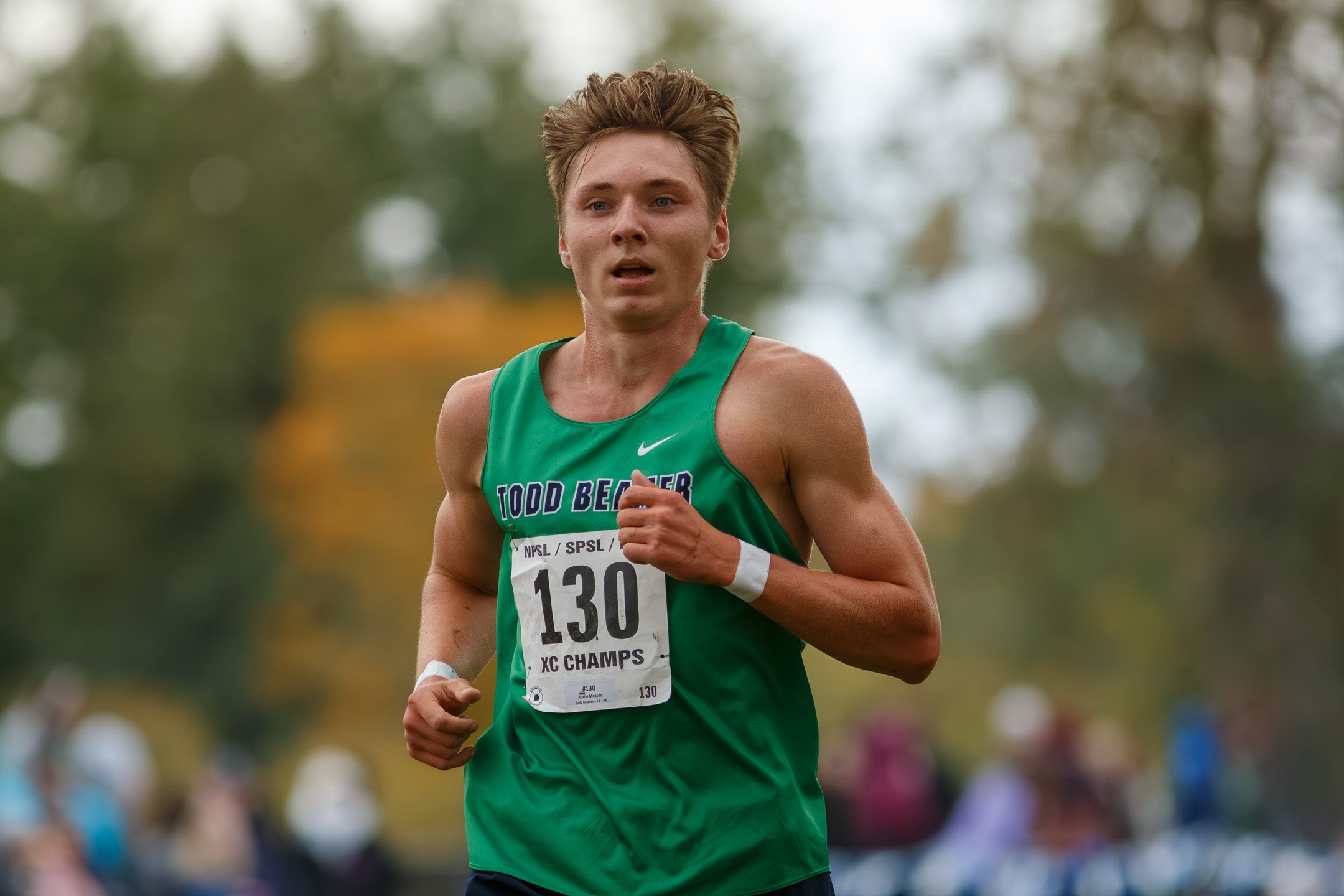 Todd Beamer senior Austin Messer, bib 130, in a green Todd Beamer singlet with white wristbands, running with spectators blurred behind him.