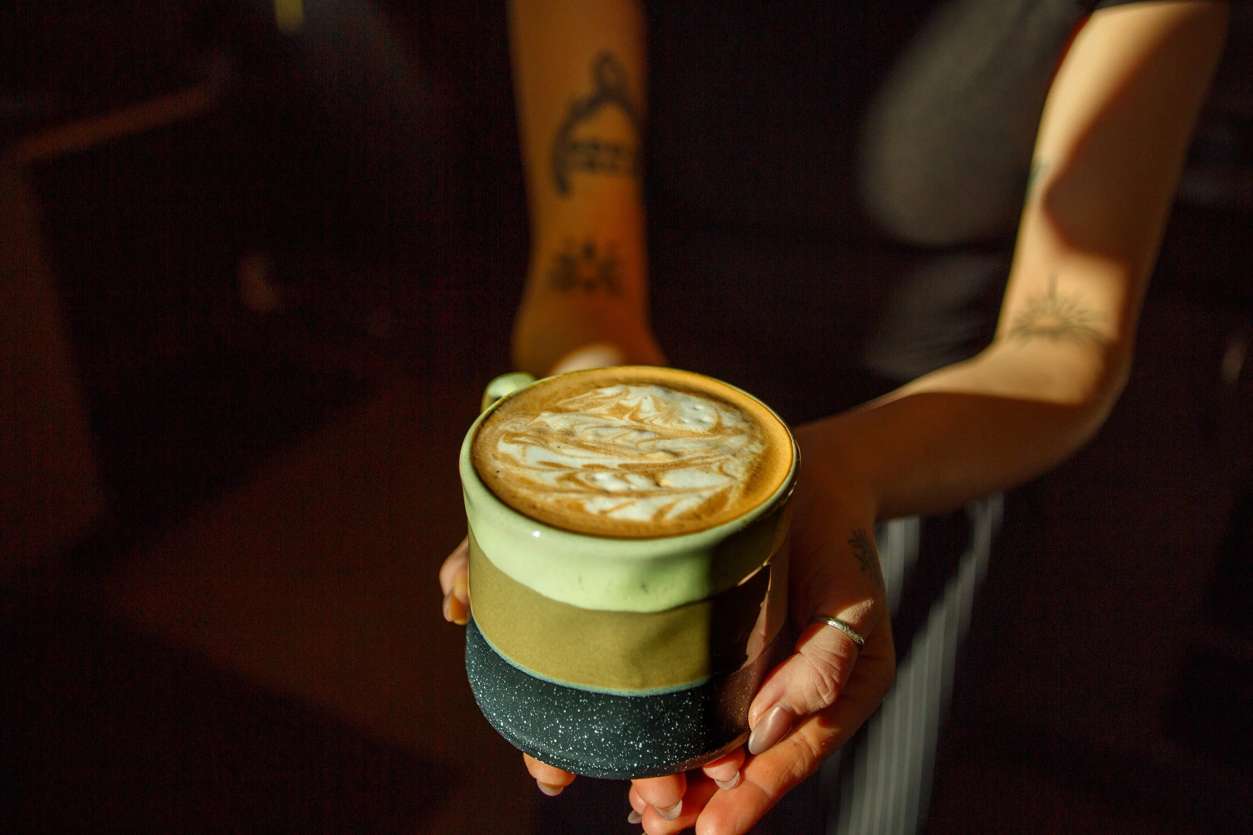 Close-up shot of a barista holding a crafted latte, representing authentic lifestyle photography in a coffee shop setting.