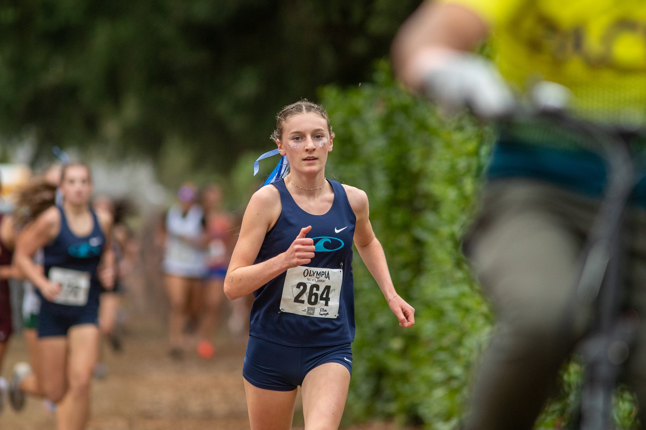 High school girl in a Gig Harbor singlet running past trees.