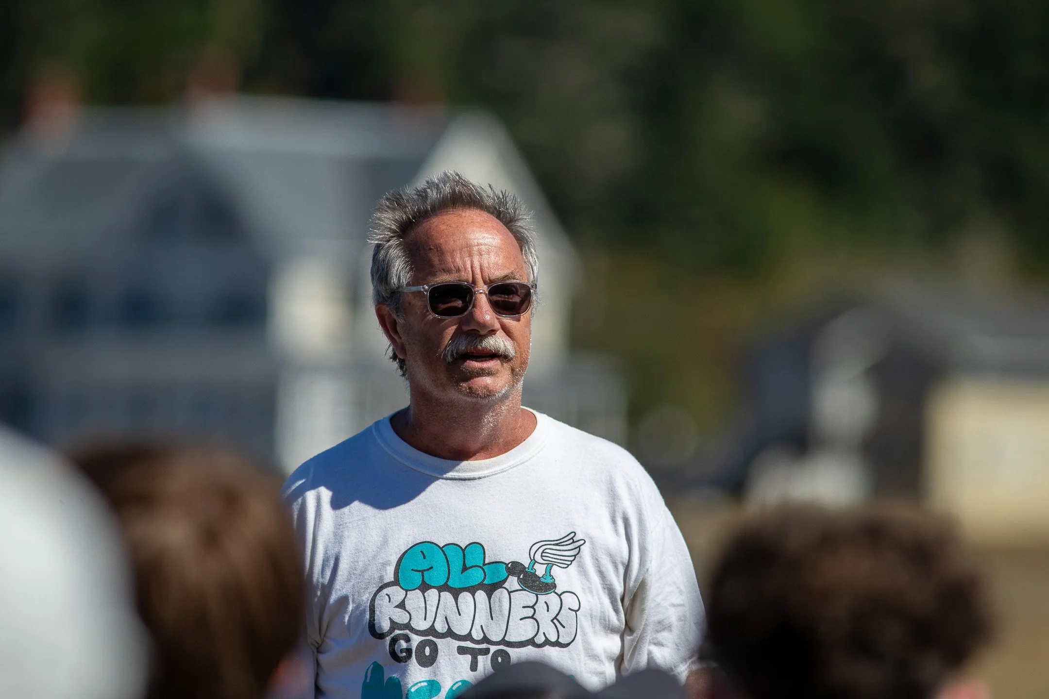Youth Runner Magazine publisher Dan Kesterson speaks to high school cross country runners and coaches seated at outdoor picnic tables during the closing awards ceremony at Fort Casey.
