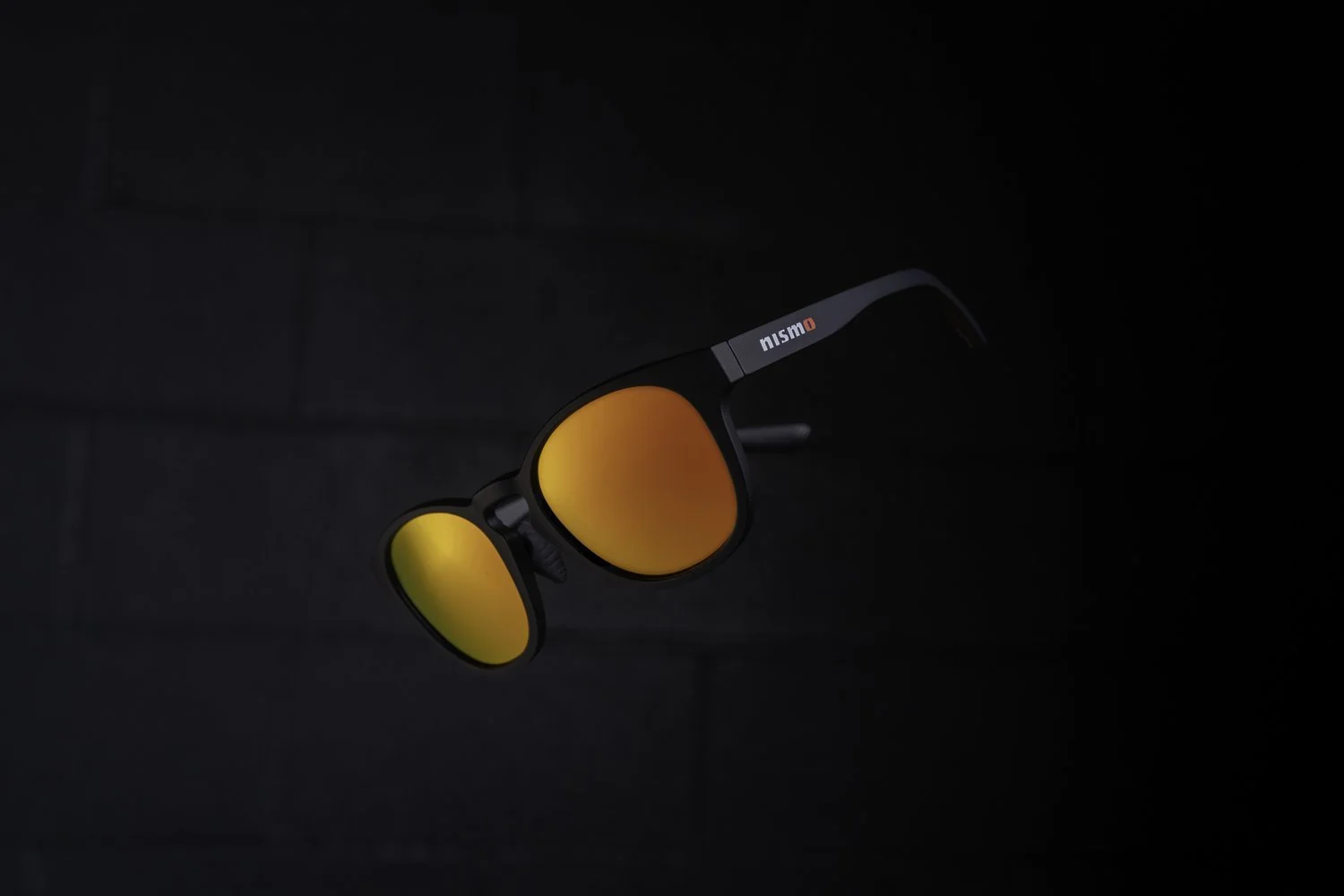 Pair of sunglasses with orange mirrored lenses and black frame against a dark background