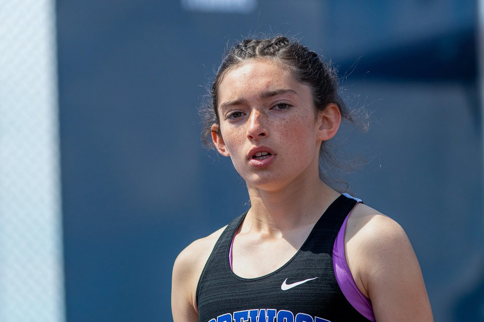 A female athletes stands with a black nike singlet that reads shorewood in blue. She has braded hair and is preparing for the start of a race.