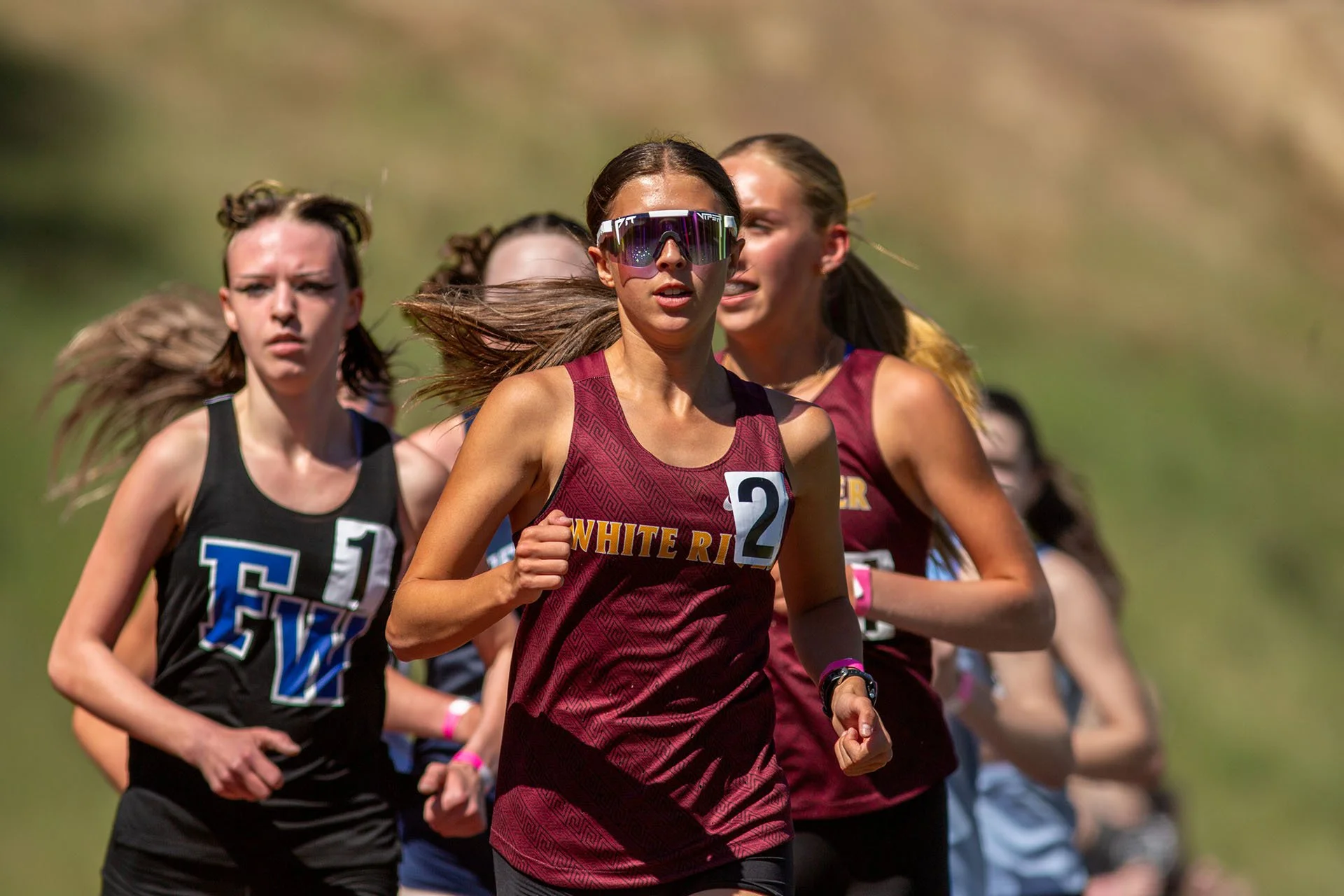 White River track athlete Paeton Poelman wearing a maroon singlet and large reflective athletic sunglasses running at the front of a tight pack in the 3200m race.