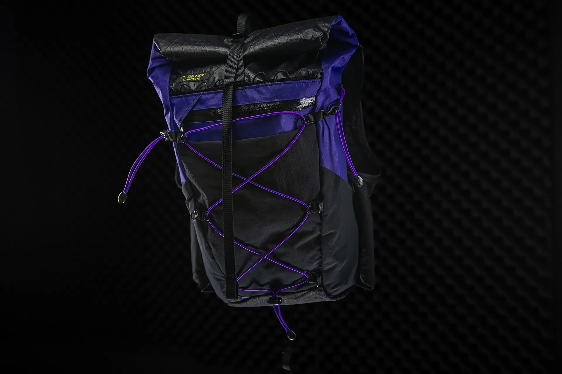 E-commerce product presentation of a black and volt purple technical gear pack against a dark grid studio background.