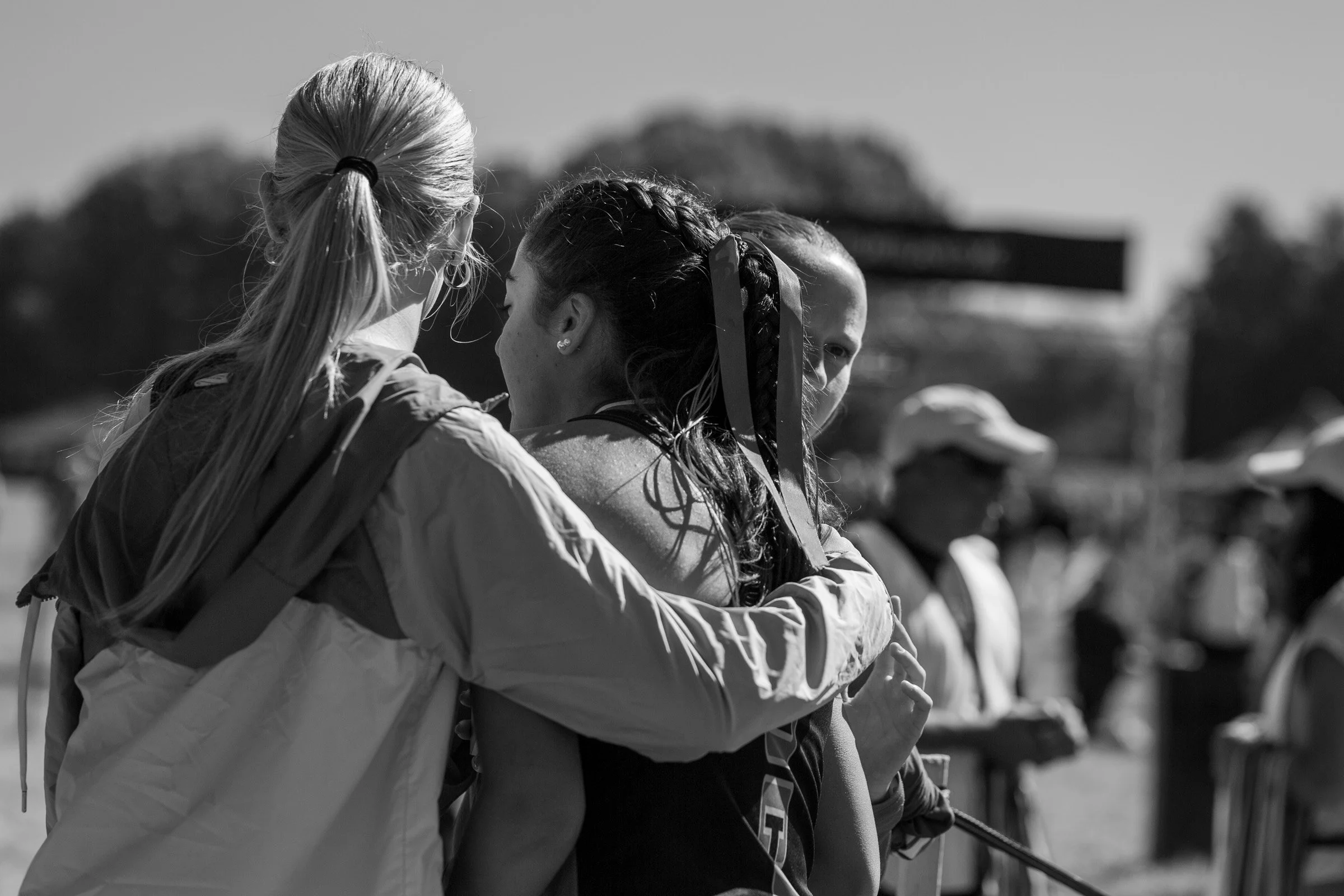 Two cross country runners hugging after a race, spectators blurred behind them.