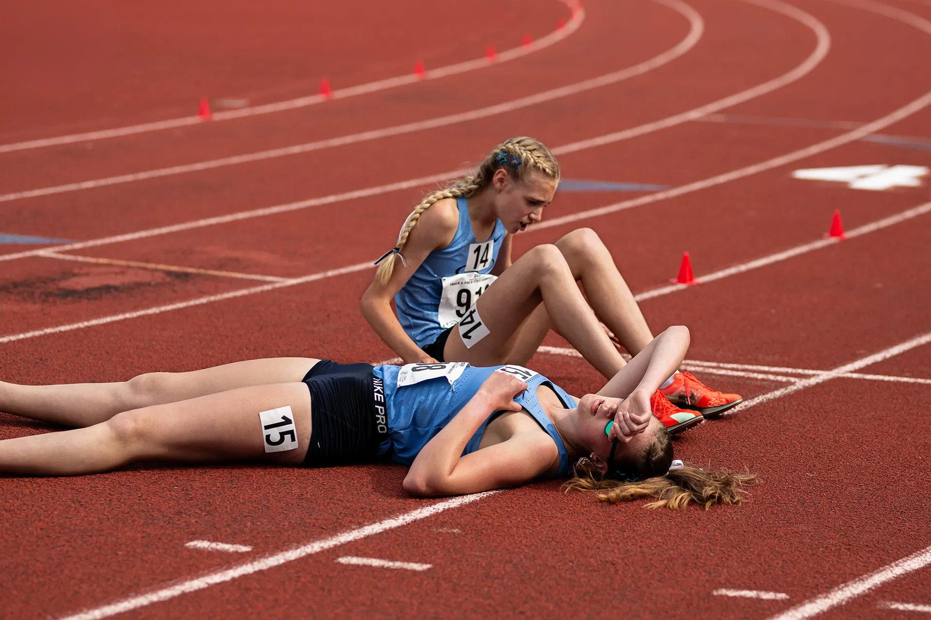 Gig Harbor track athletes Maya Crane and Lejla Carlsson sit on the red track surface, resting after completing the girls 3A 1600M race.