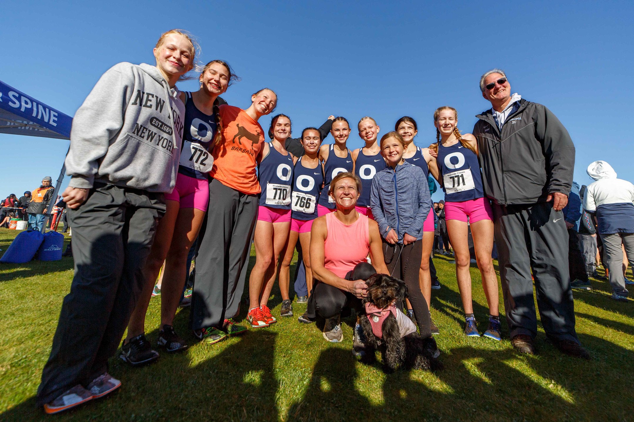 Olympia girls varsity cross country team posing with their coaches and a dog after the 2025 Westside Classic