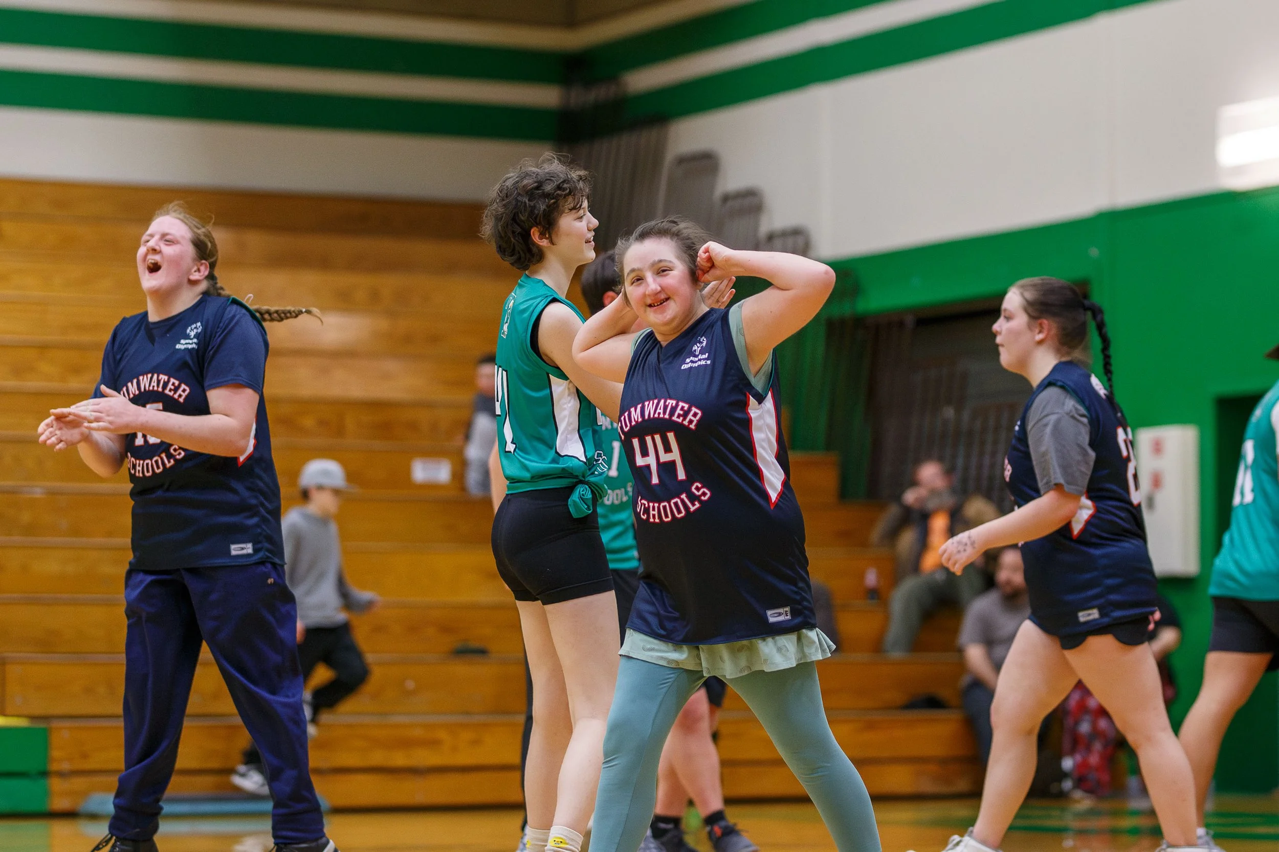 A Tumwater High School Unified Basketball athlete (number 44) flexes their arms in triumph while a teammate cheers excitedly in the background during a game against Black Hills High School.