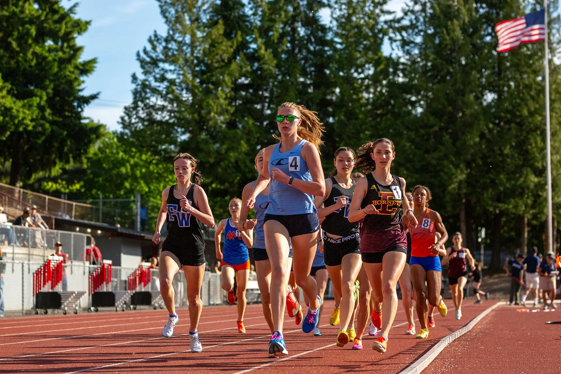 Gig Harbor's Lejla Carlsson in a light blue singlet and green mirrored sunglasses leading a tight pack of female runners on a red track during the 3A 1600m race.