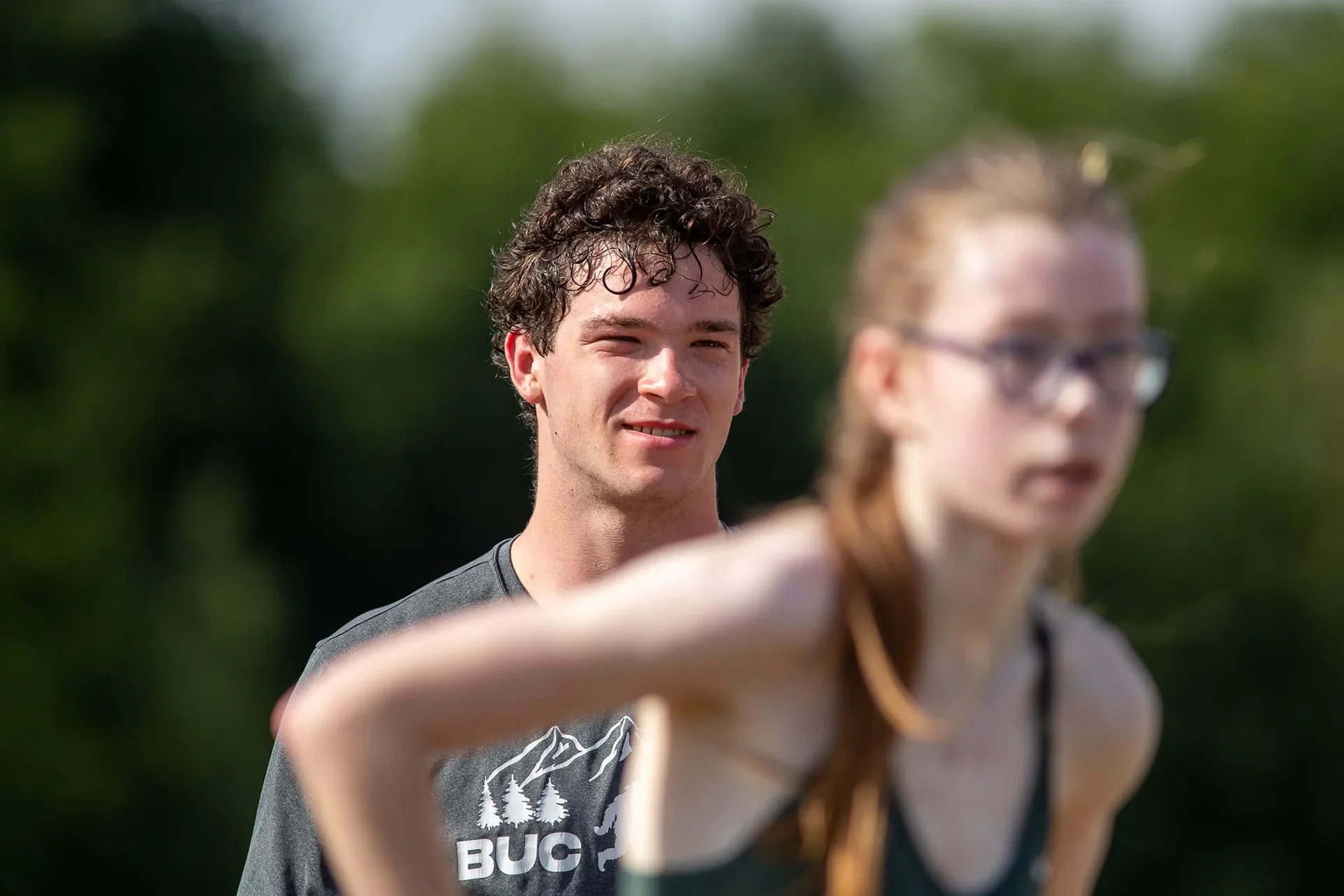 A sweaty teenage boy, Coen Van Vliet, looking exhausted but smiling after a run, with a blurred teenage girl, Emma Grice, in the foreground.