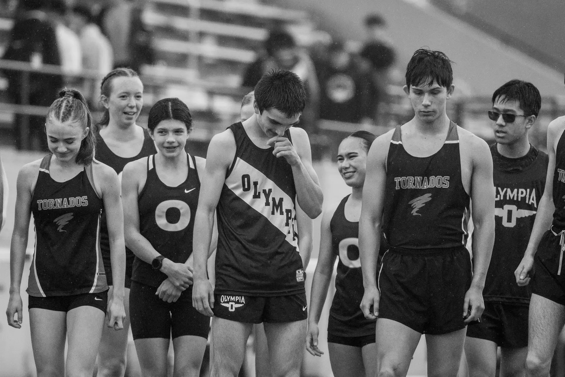 A black and white photo of male and female track athletes wearing Olympia and Yelm uniforms at a high school track meet in Olympia, WA, photographed by Russell Moore.