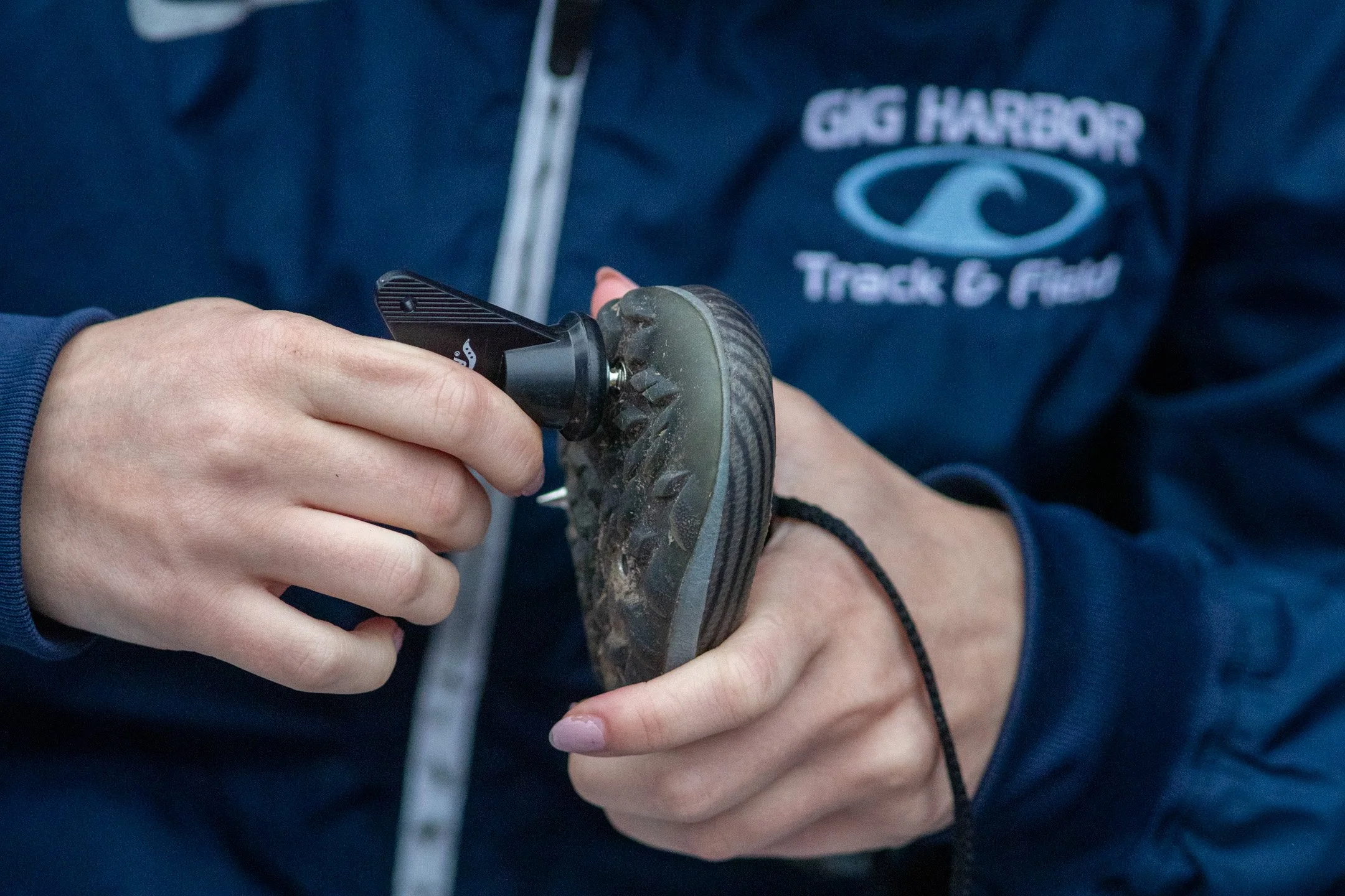 Close-up shot of a runner's hands using a black spike wrench to install metal spikes into a cross country running shoe.