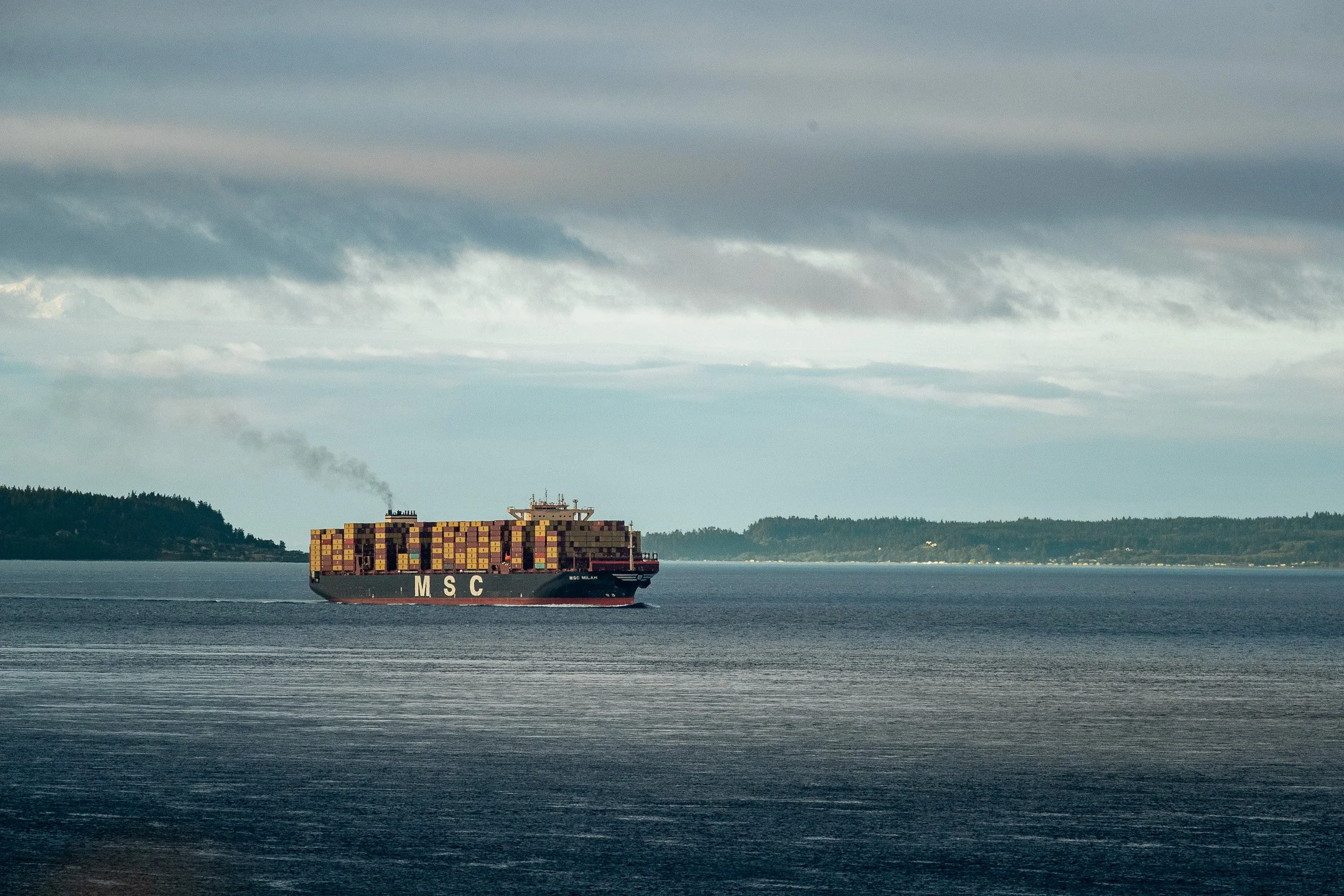 Scenic wide shot of a commercial cargo ship gliding across Admiralty Inlet with the Olympic Peninsula mountains in the distance, viewed from the bluffs above Camp Casey.