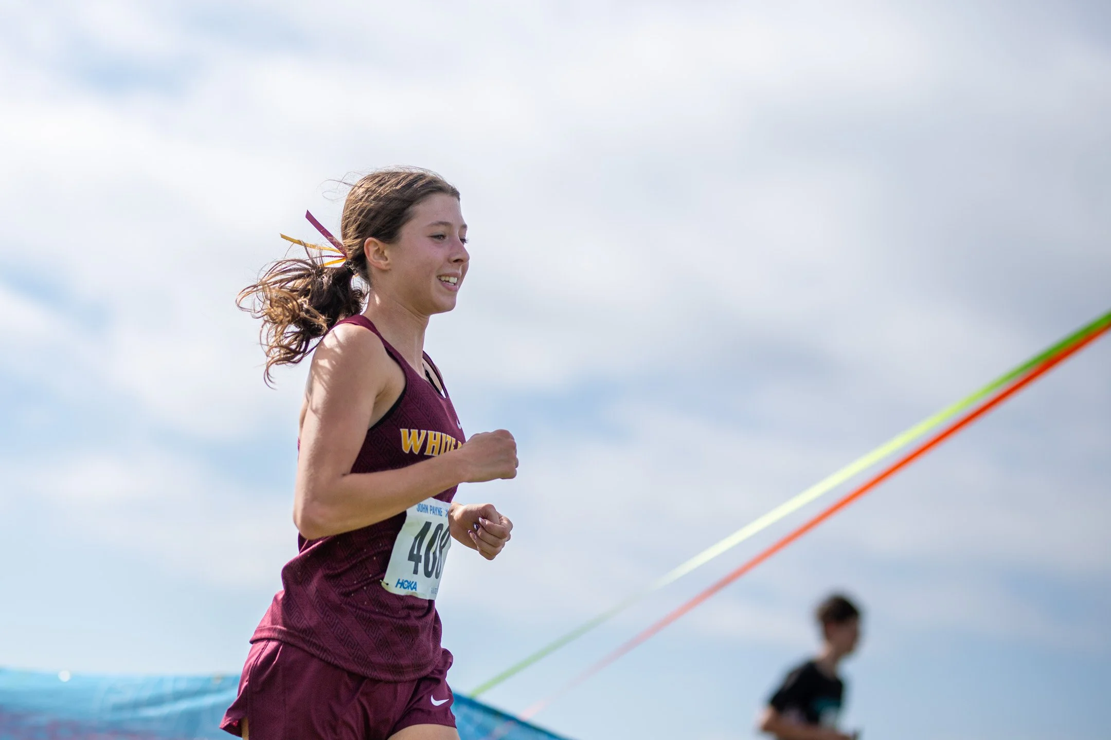 White River runner Paeton Poelman smiling as she sprints through the final meters of the race toward the finish line.