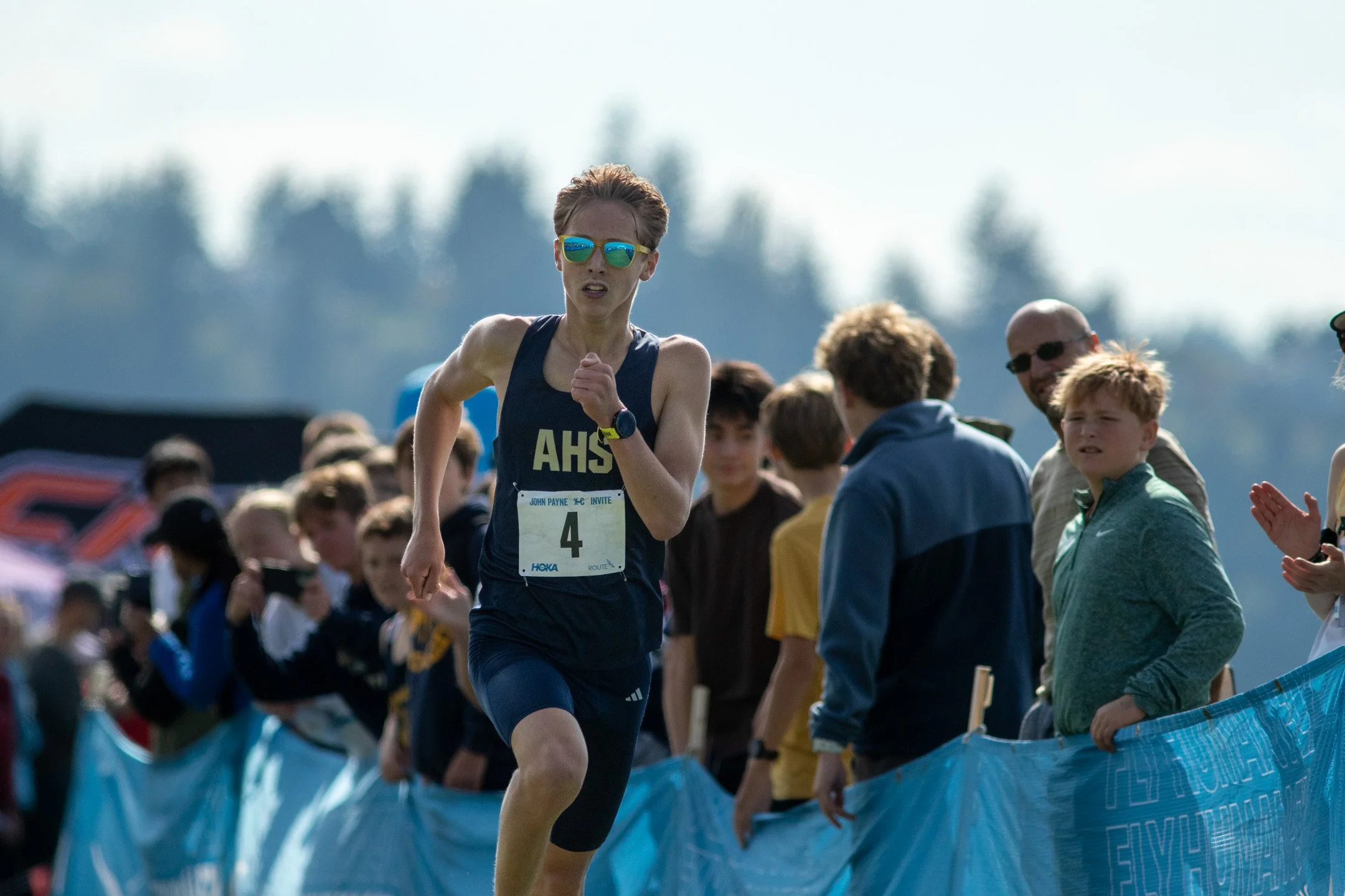 Arlington runner Chase Koenigs wearing sunglasses and a navy blue jersey with bib 4 running hard down the finishing chute.