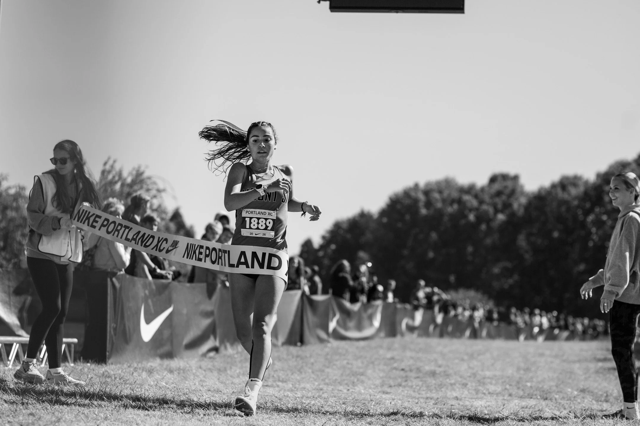 Black-and-white image of Mt. Si's Sophia Rodriguez running through the Nike Portland XC finish tape, held by Lincoln High's Ellery Lincoln.