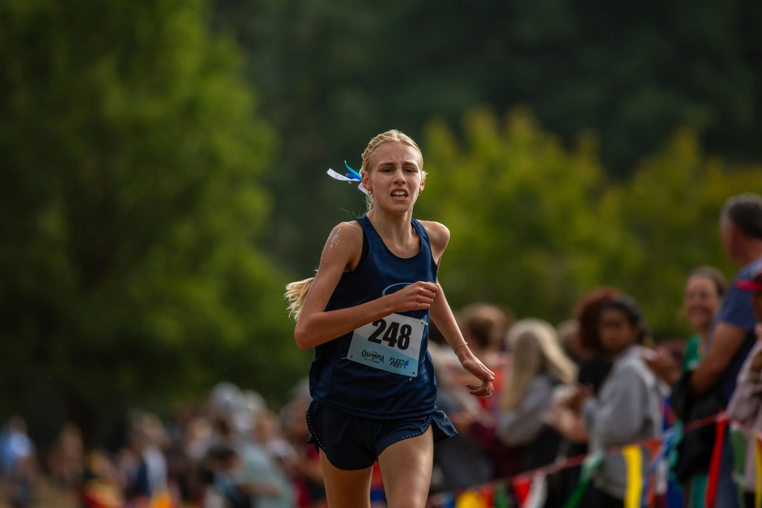 Girl in navy Gig Harbor jersey, bib 248, straining through the finish with spectators lining the course.