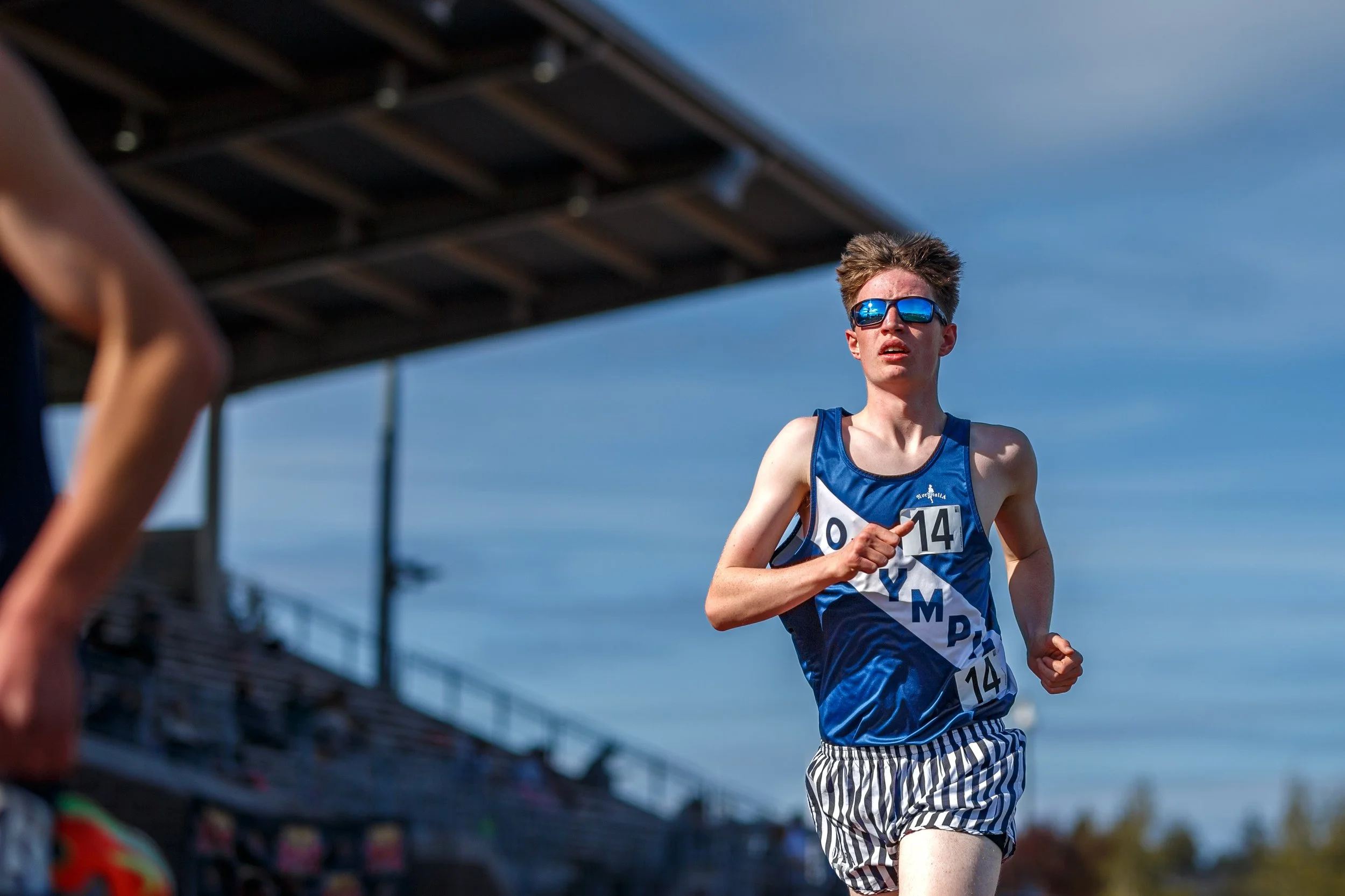 James Levitt of Olympia High School running on the track, wearing a navy Olympia singlet and sunglasses.