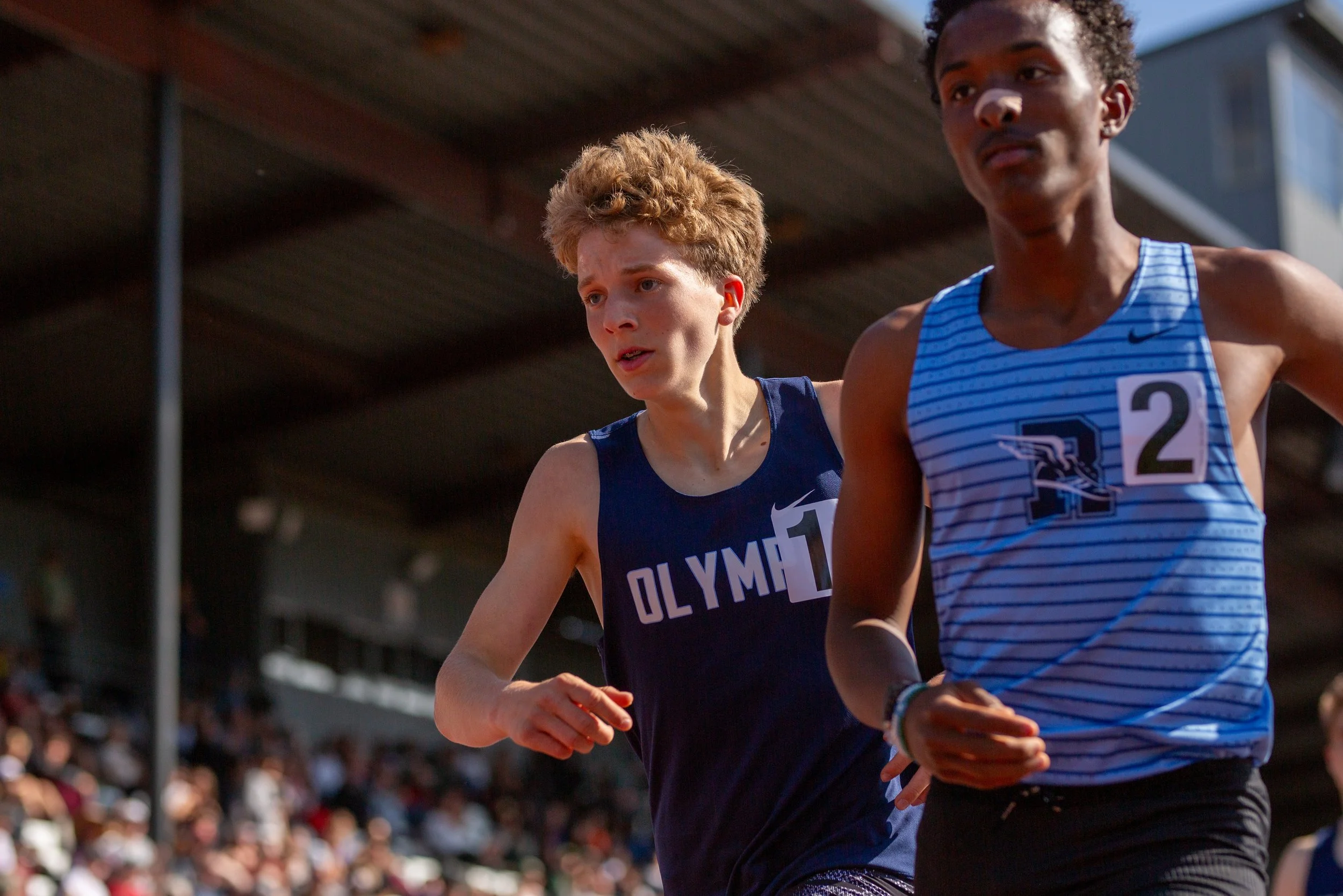 Olympia freshman Quenton Lanese in a dark blue singlet running shoulder-to-shoulder just behind Rogers senior Amin Fidaar in a light blue striped singlet during the 4A Boys 1600m race.