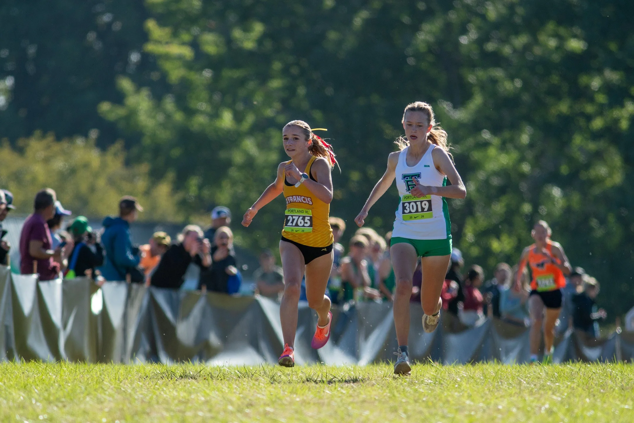 St. Francis's Ellison Williams in yellow and ThunderRidge's Jetta Betts in white and green run side by side past spectators.