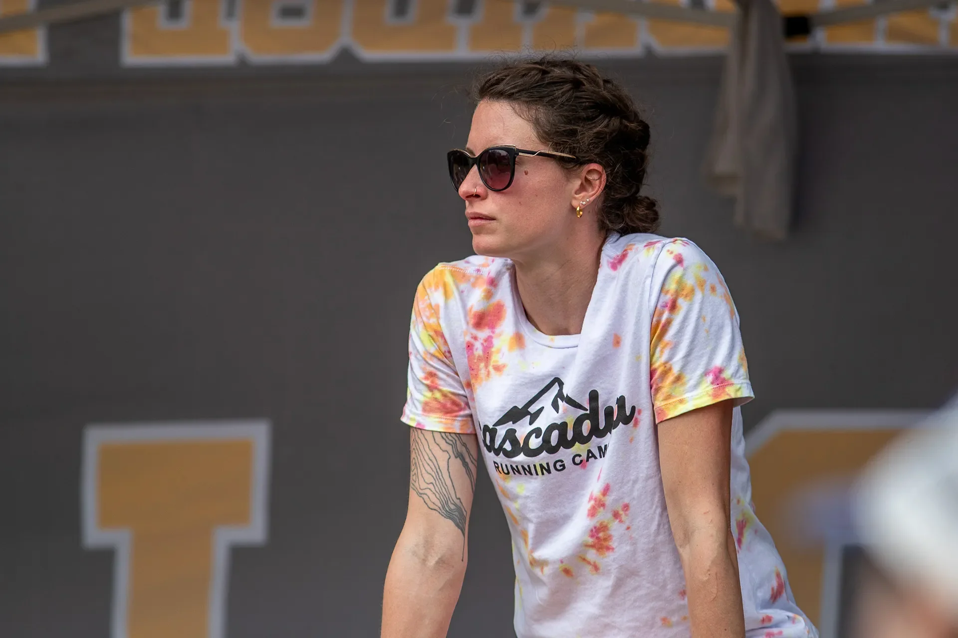 Jena Winger wearing sunglasses and a colorful tie-dye Cascadia Running Camp t-shirt looking out across the campsite.