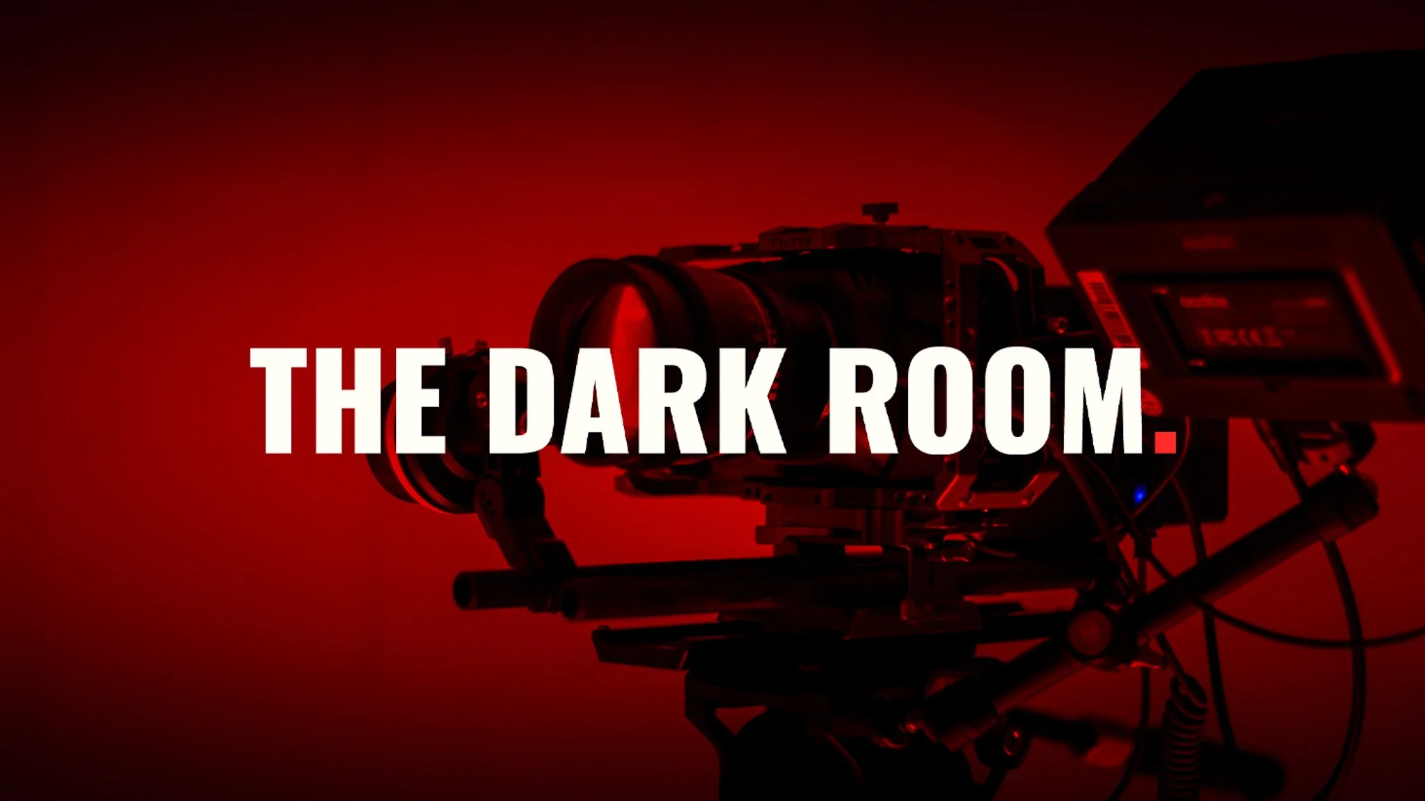 A professional BMPCC4K camera rig on a tripod, illuminated by intense red light, with the bold white text 'THE DARK ROOM.' centered across the frame.