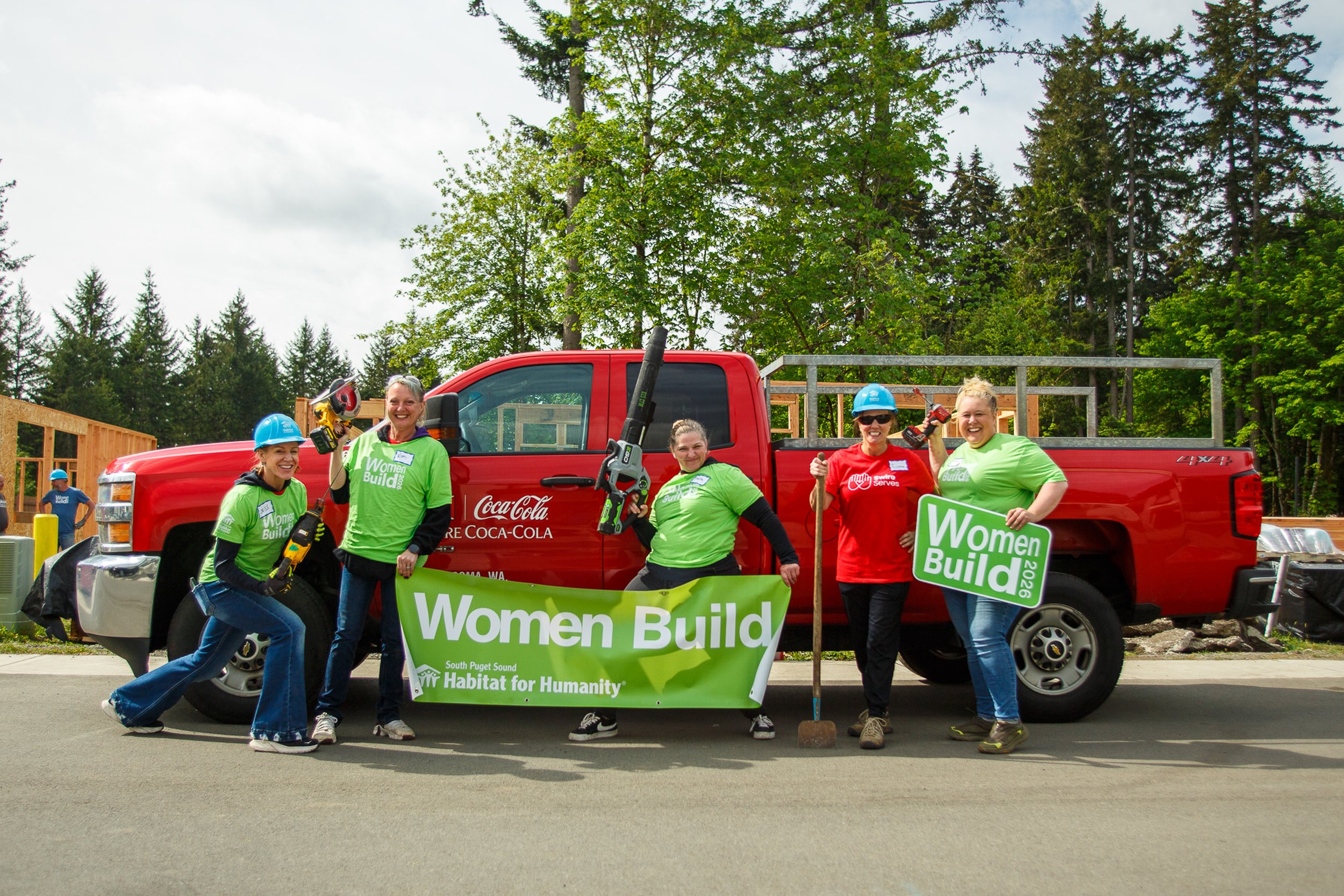 A group of smiling volunteers posing together in front of a red Swire Coca-Cola delivery truck at a construction site.