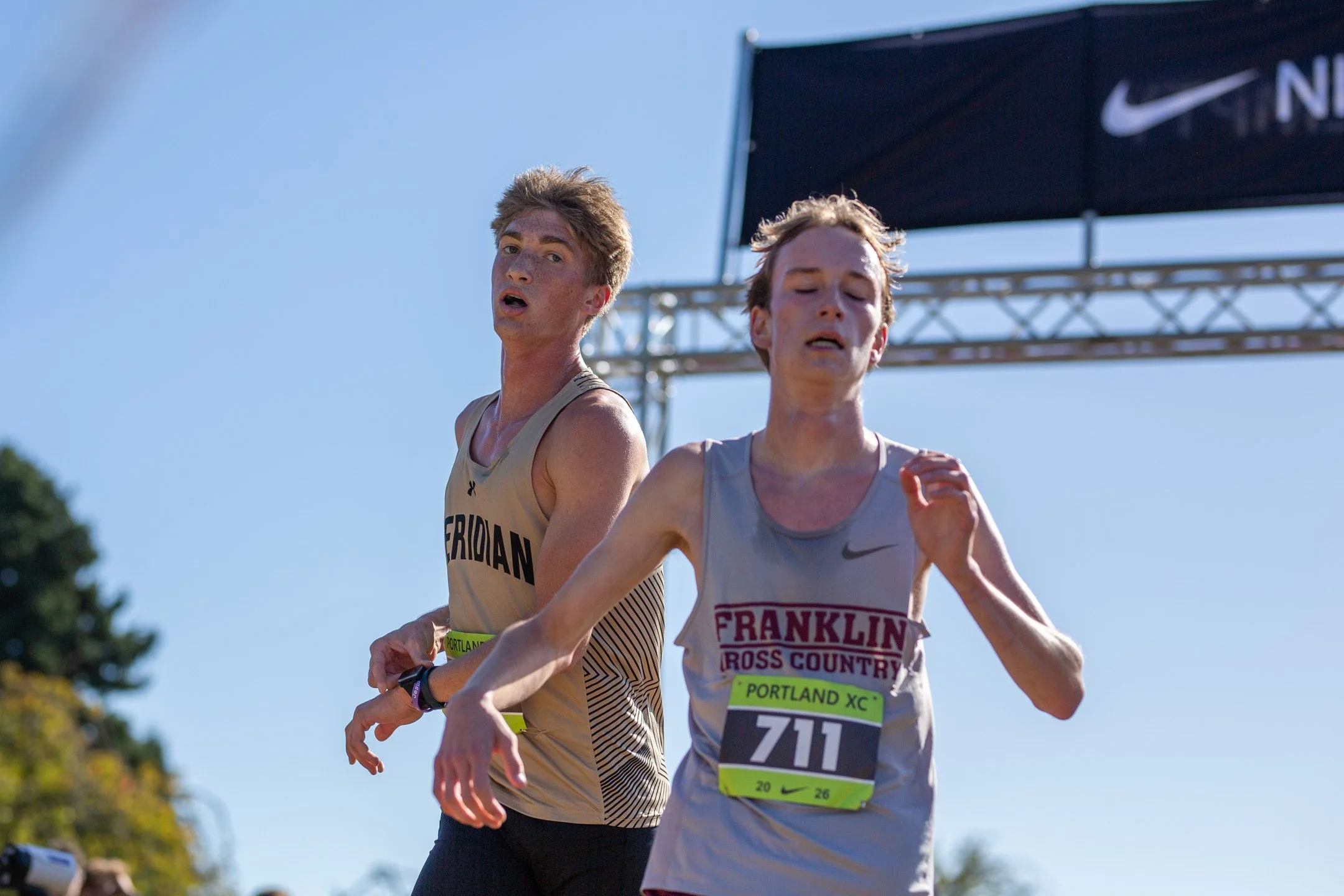 Meridian's Judah TeVelde, left, and a Franklin runner stride side by side toward the finish beneath the Nike banner.