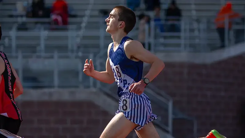 Jack McDurmon of Olympia High School competing in a track race, wearing a navy and white striped uniform.
